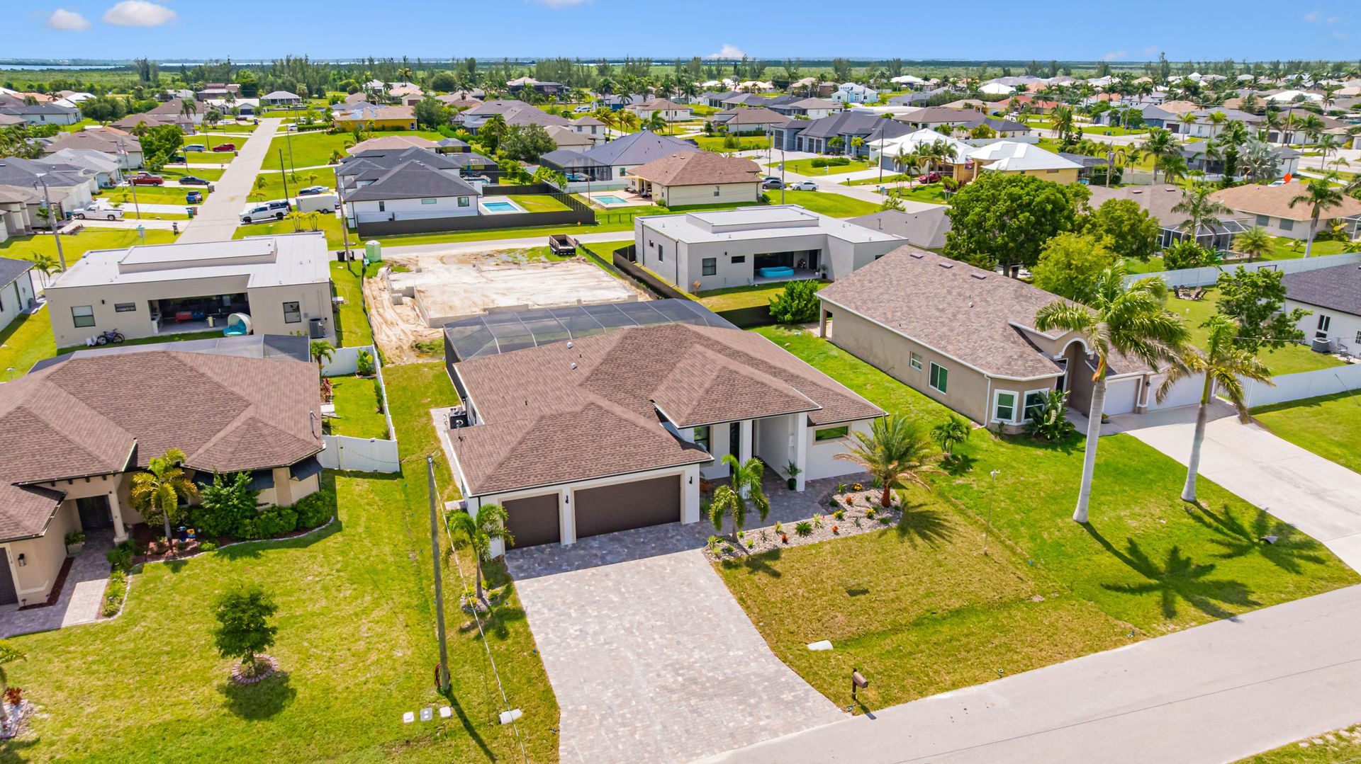 Aerial view of suburban homes with driveways and green lawns. Blue sky overhead.