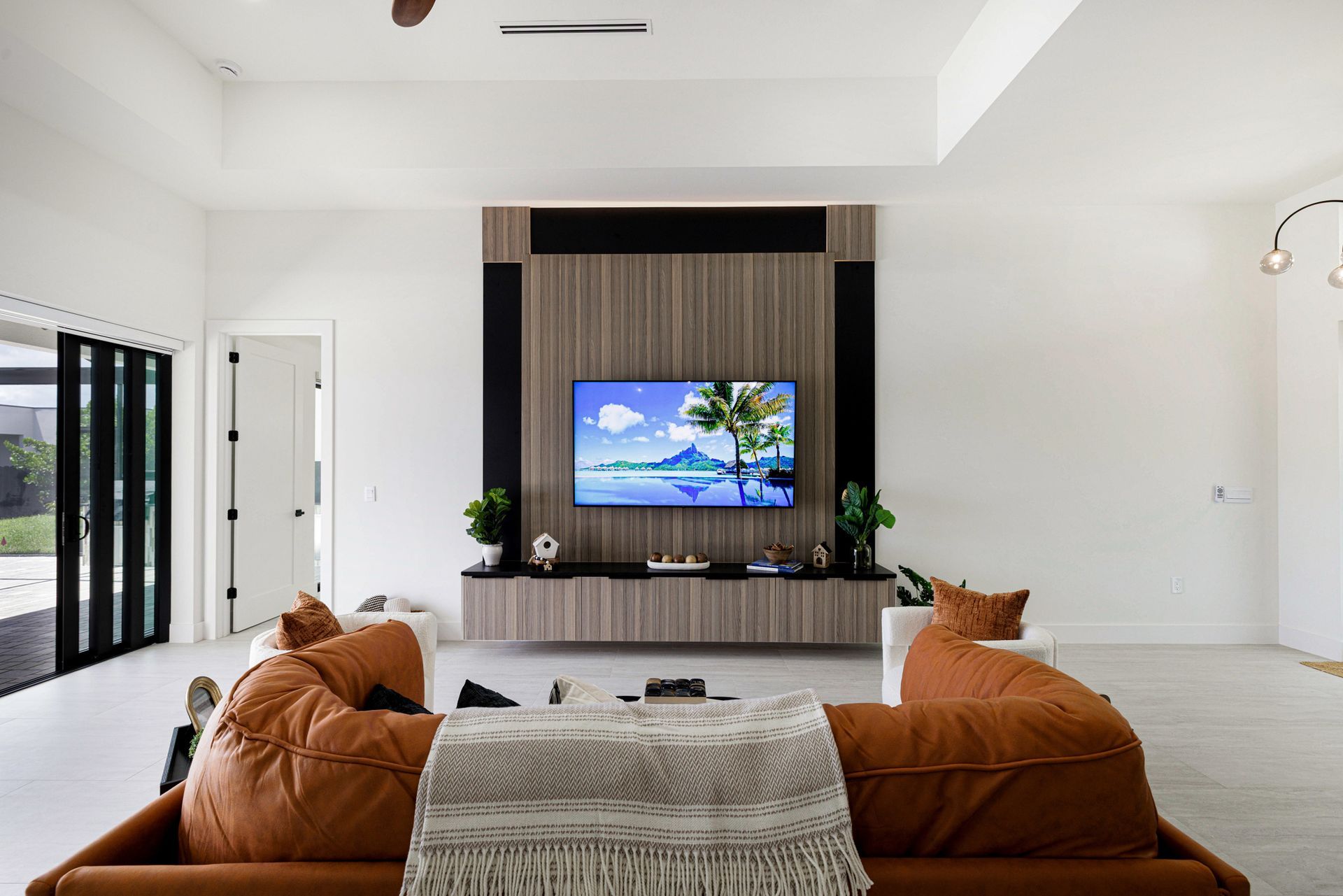 Spacious living room with a large TV on a wood-paneled wall. Brown modular seating, bright white walls.