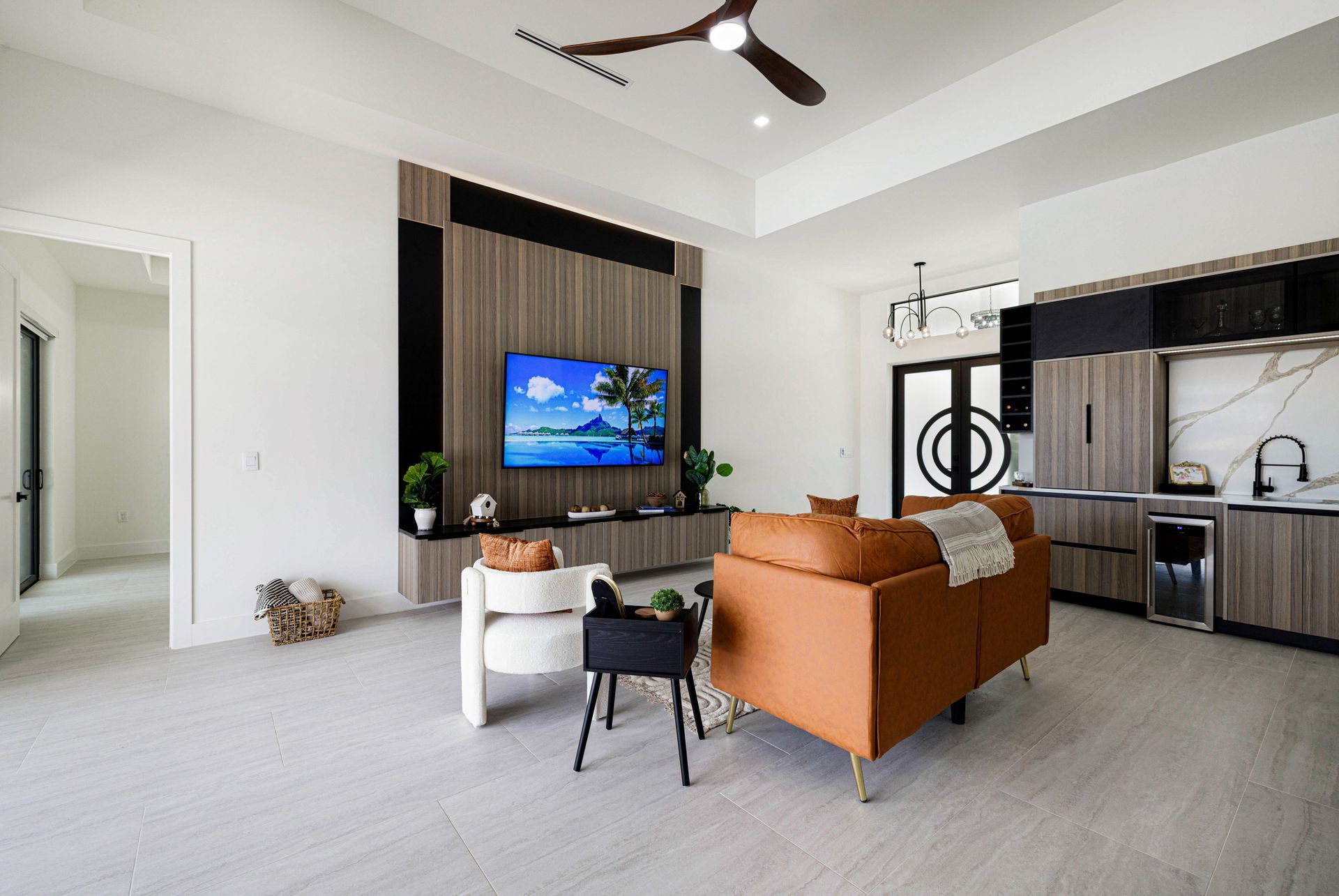 Modern living room with brown and white furniture, TV, and kitchen in the background.