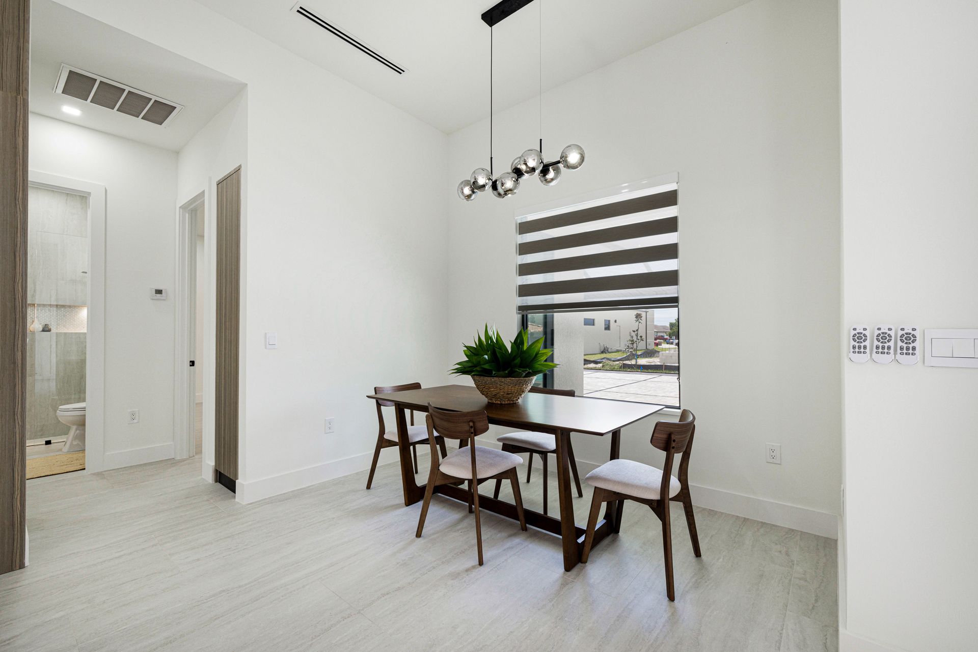 Dining area with table and chairs, plants, modern light fixture, window with blinds.