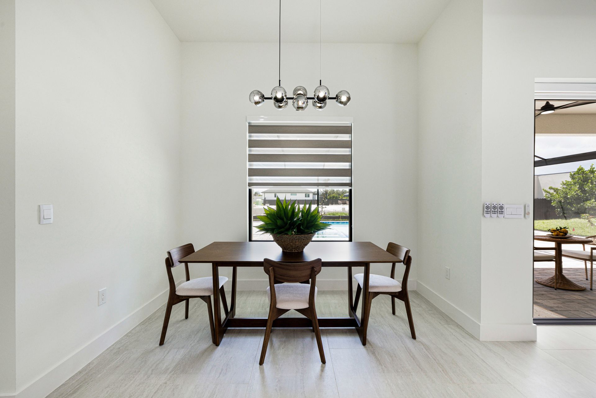 Dining room with table, chairs, large plant, chandelier, and window overlooking patio.