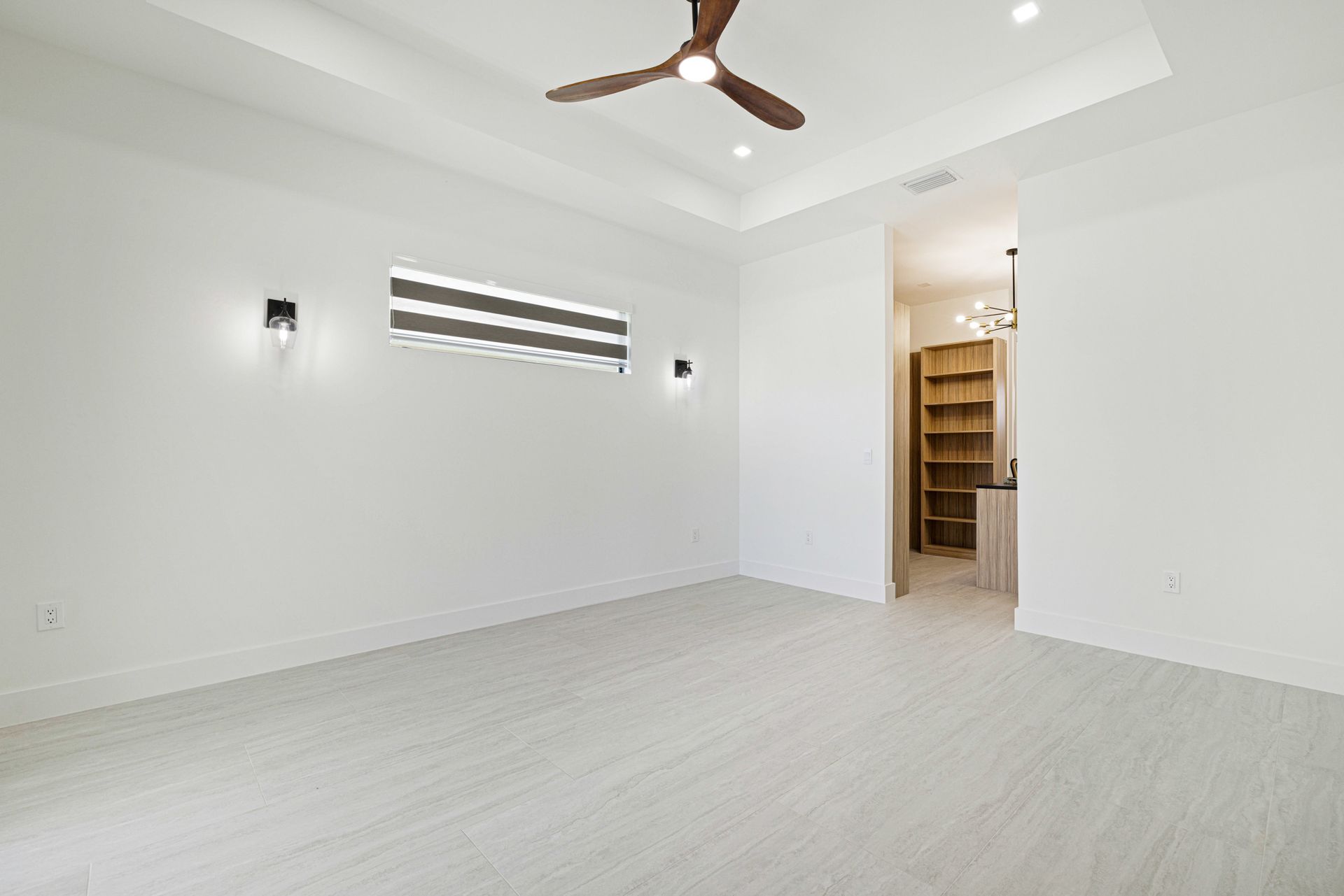 Empty, white-walled room with light wood-look flooring. Ceiling fan, recessed lighting, and a doorway leading to storage.