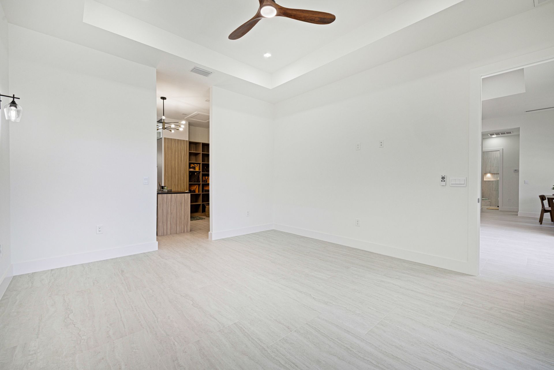 Empty white room with light wood floors, ceiling fan, and doorway to walk-in closet.