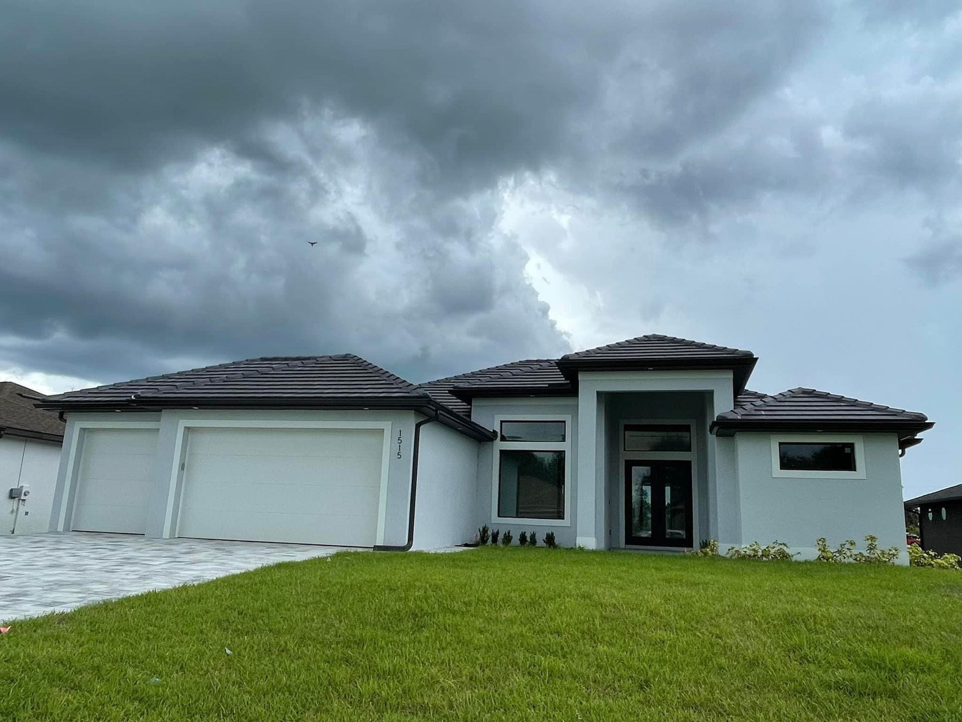 Modern light blue house with white garage doors, and dark gray roof, under a cloudy sky.