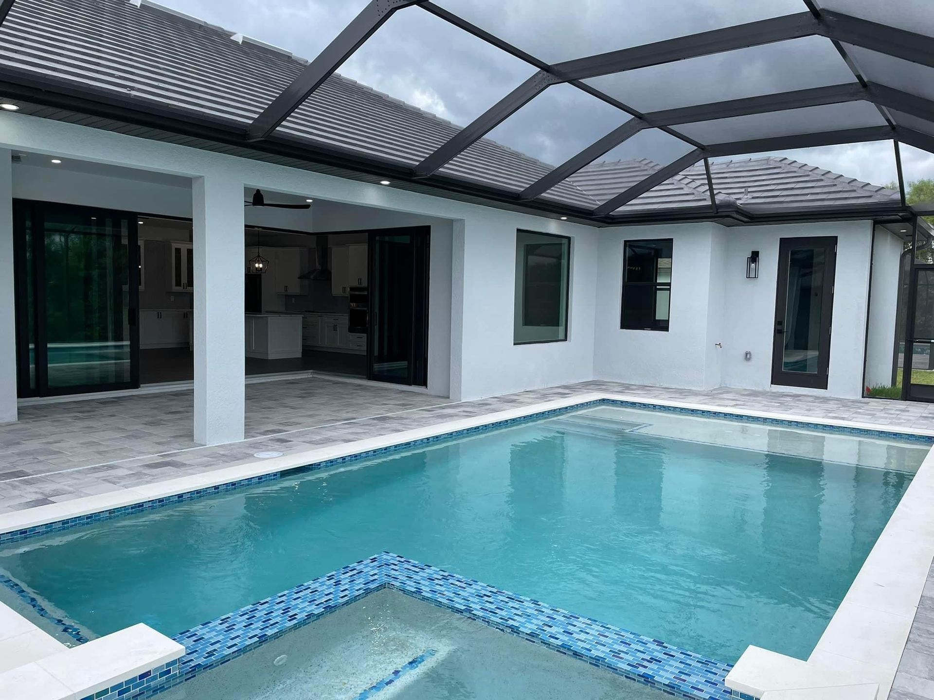 Pool area with a blue pool, patio, and retractable roof. White walls, dark trim, and clear sky.