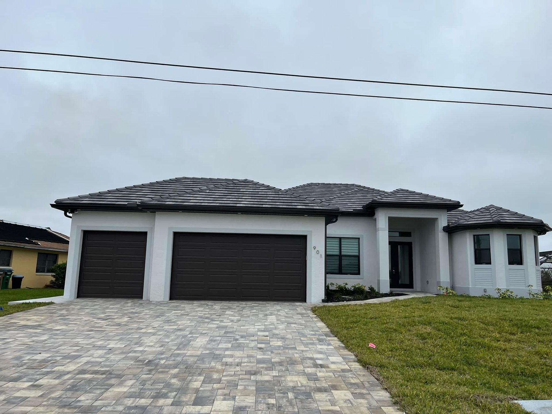 White house with dark brown garage doors and roof, paved driveway, green lawn.