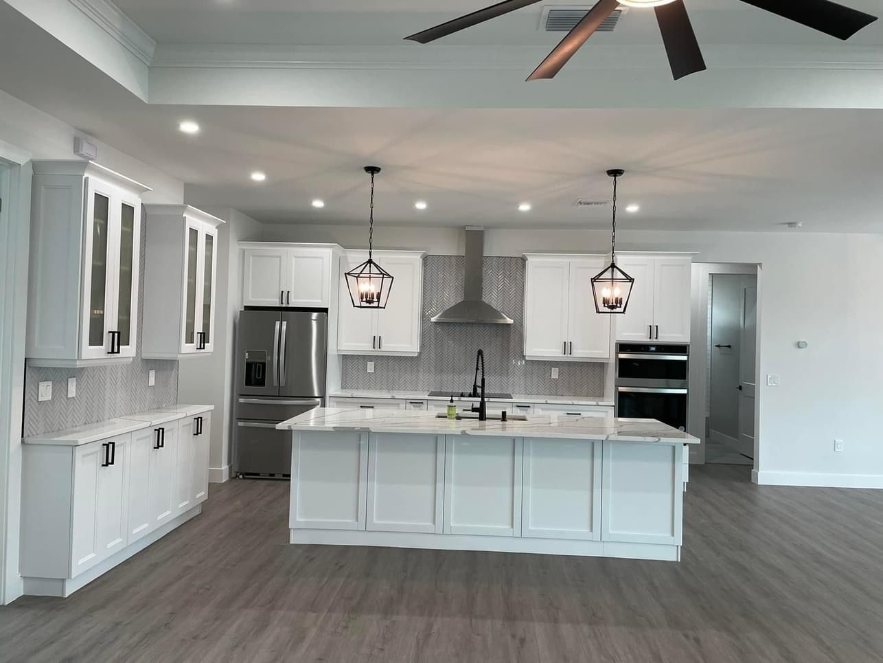 White kitchen with island, stainless steel appliances, pendant lights, and grey tile backsplash.