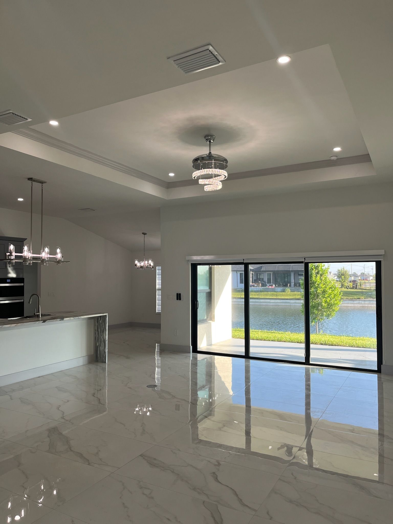 Spacious modern home interior, featuring a bright kitchen, glossy floors, and a view of a lake through sliding glass doors.