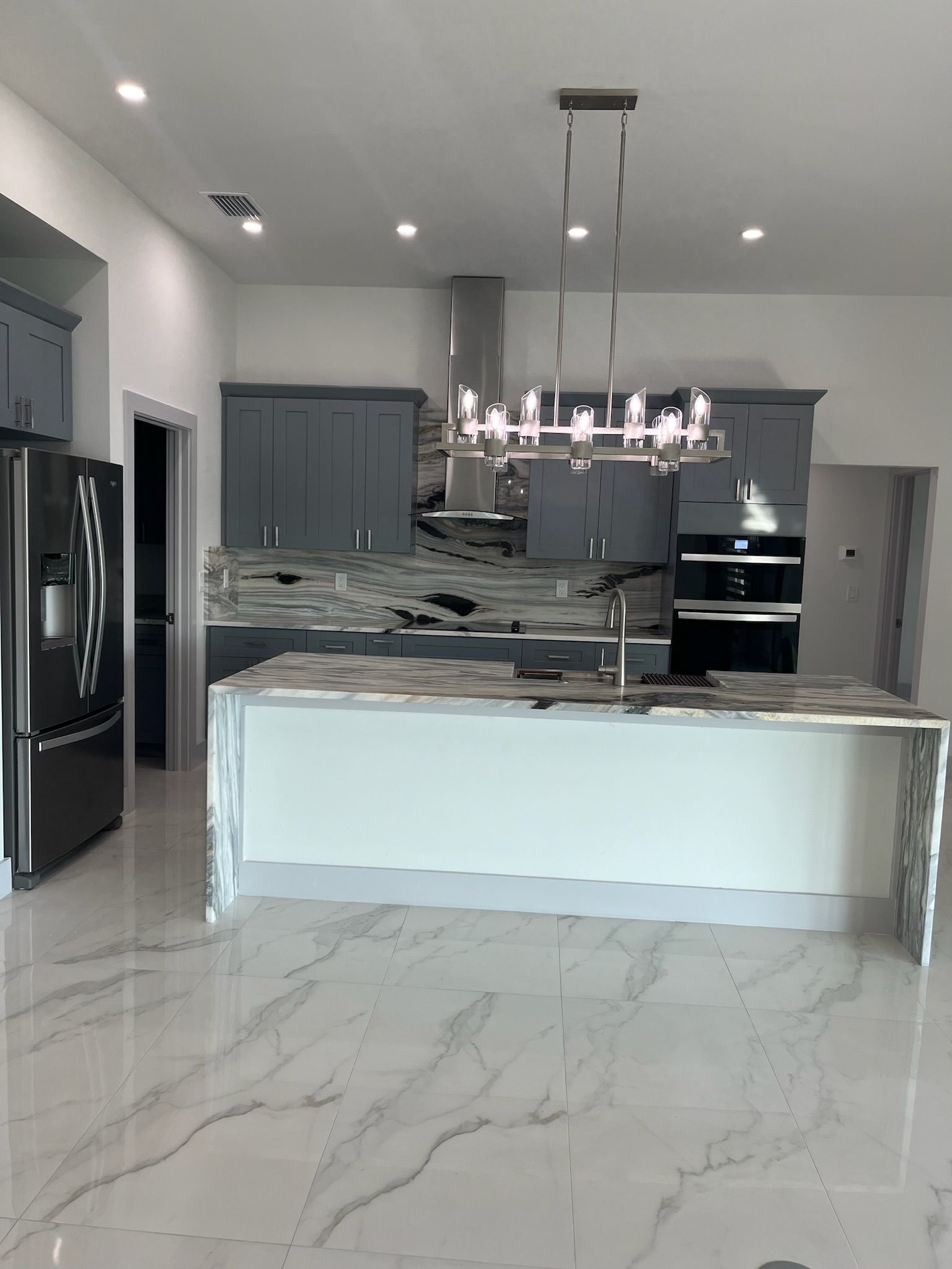 Modern kitchen with gray cabinets, marble countertops, and a large island.