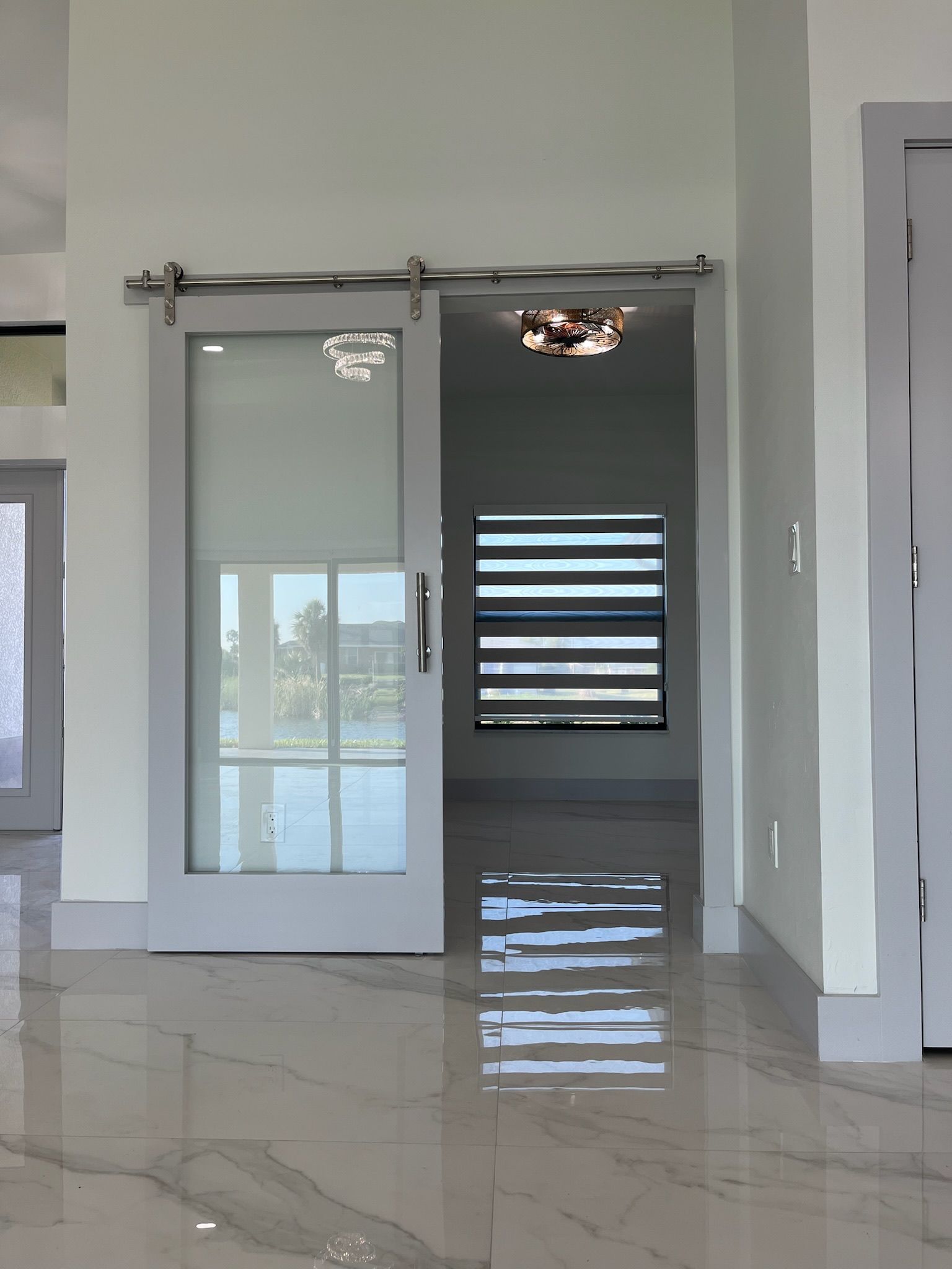 Gray sliding barn door with glass panel, facing a room with a window, and a shiny floor.