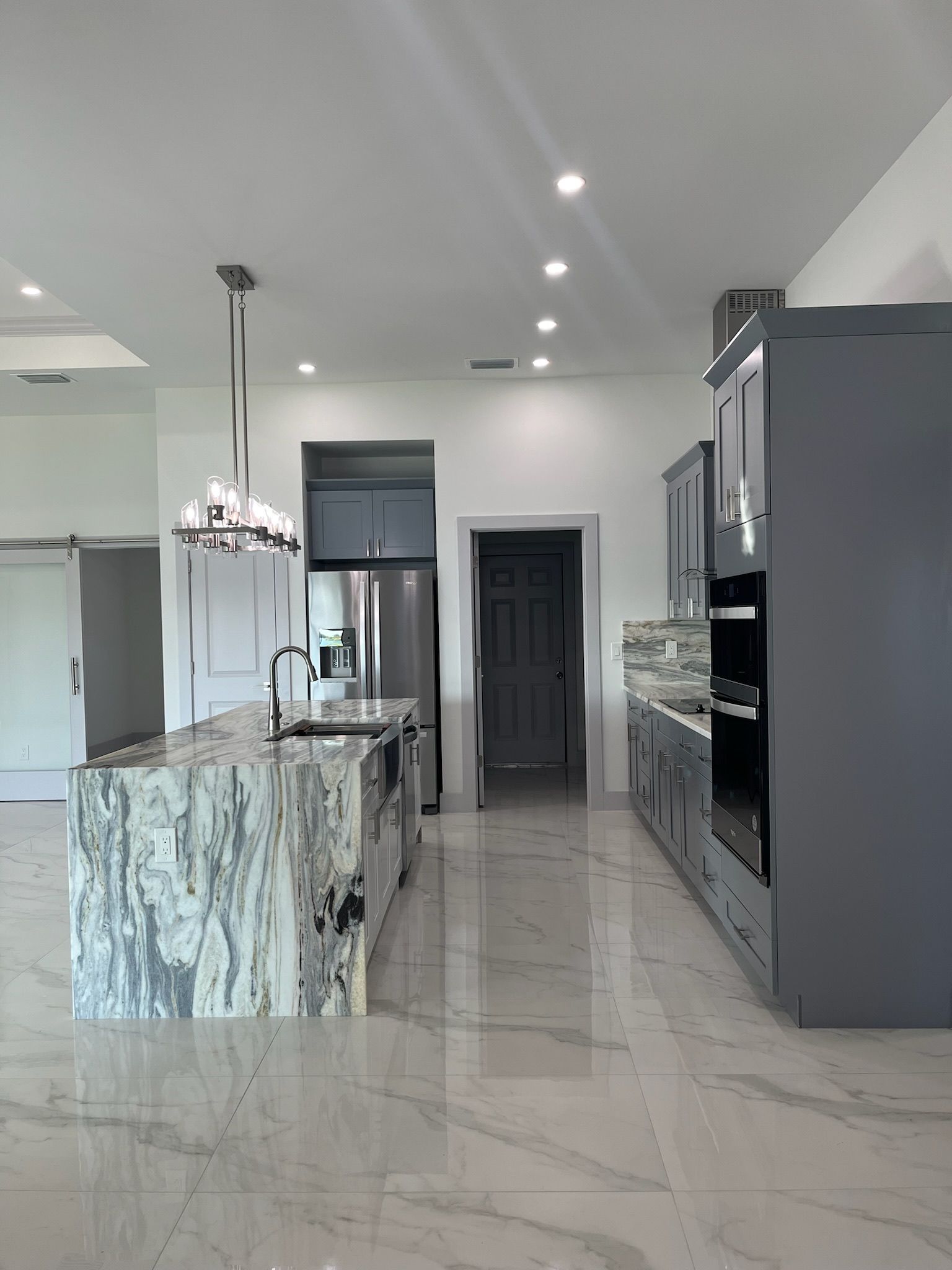 Modern kitchen with a marble island, gray cabinets, and stainless steel appliances.