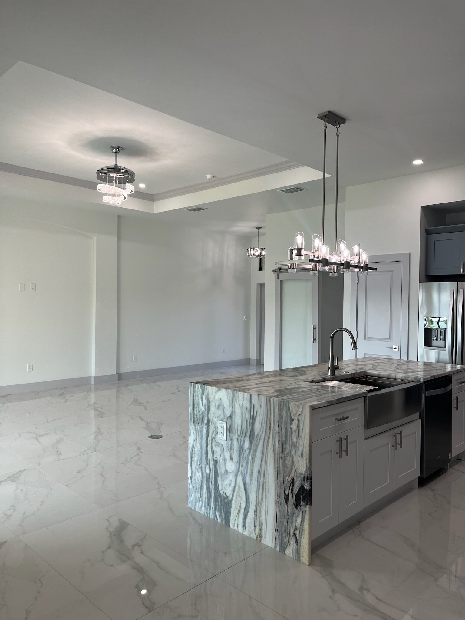 Modern kitchen with marble island, stainless steel appliances, and a living area with white walls and floors.