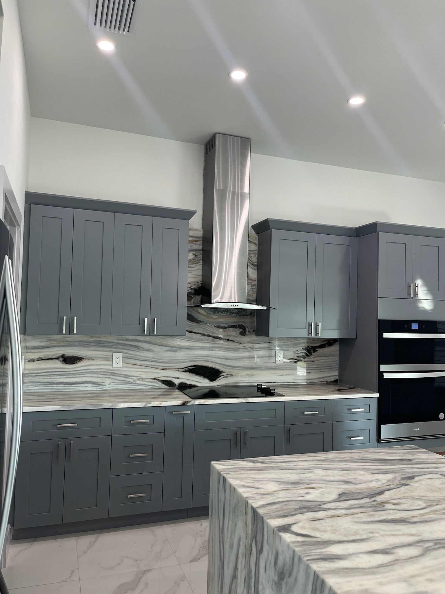 Gray kitchen with cabinets, island, stainless steel range hood, and granite countertops.