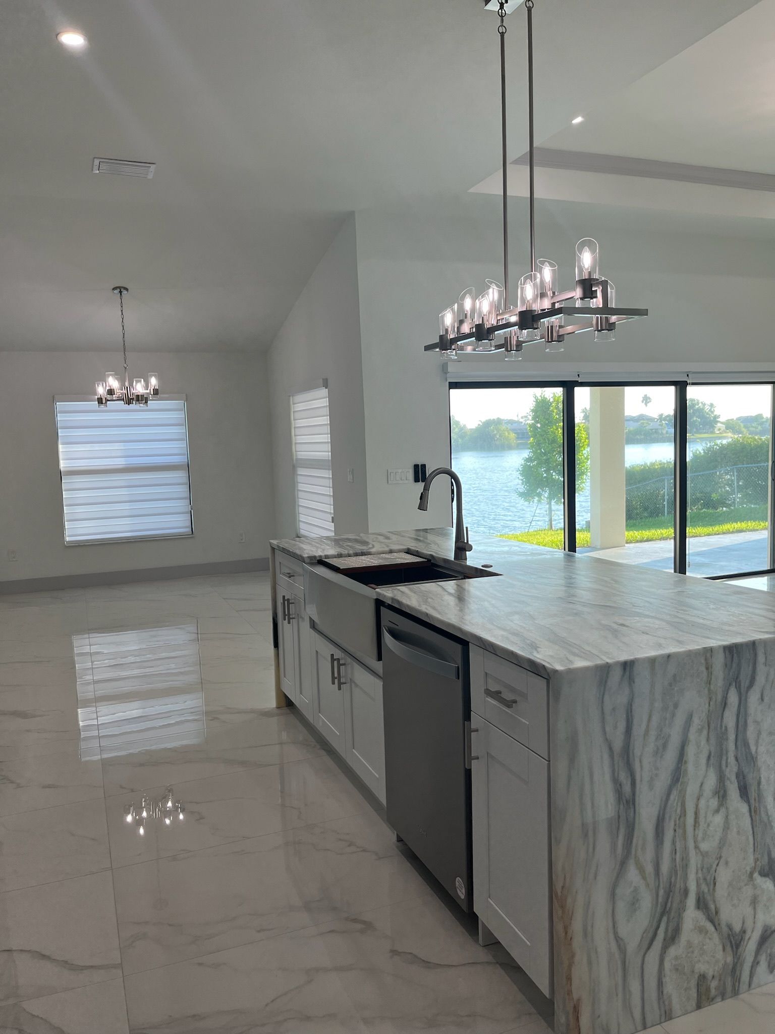 Modern kitchen with a large island, stainless steel appliances, and a view of a lake through glass doors.