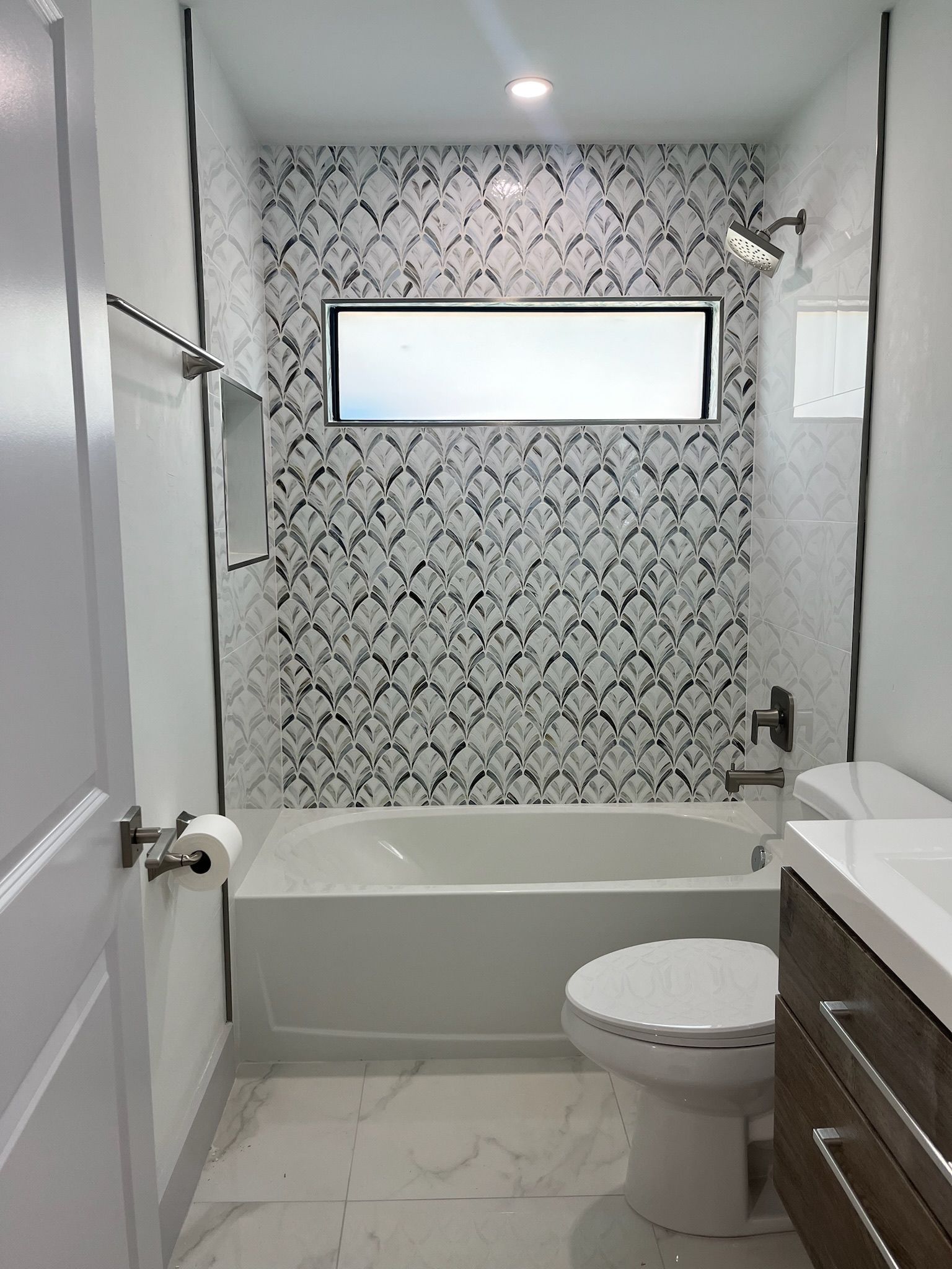 Bathroom with white tub, toilet, and sink. Backsplash has black and white patterned tiles.
