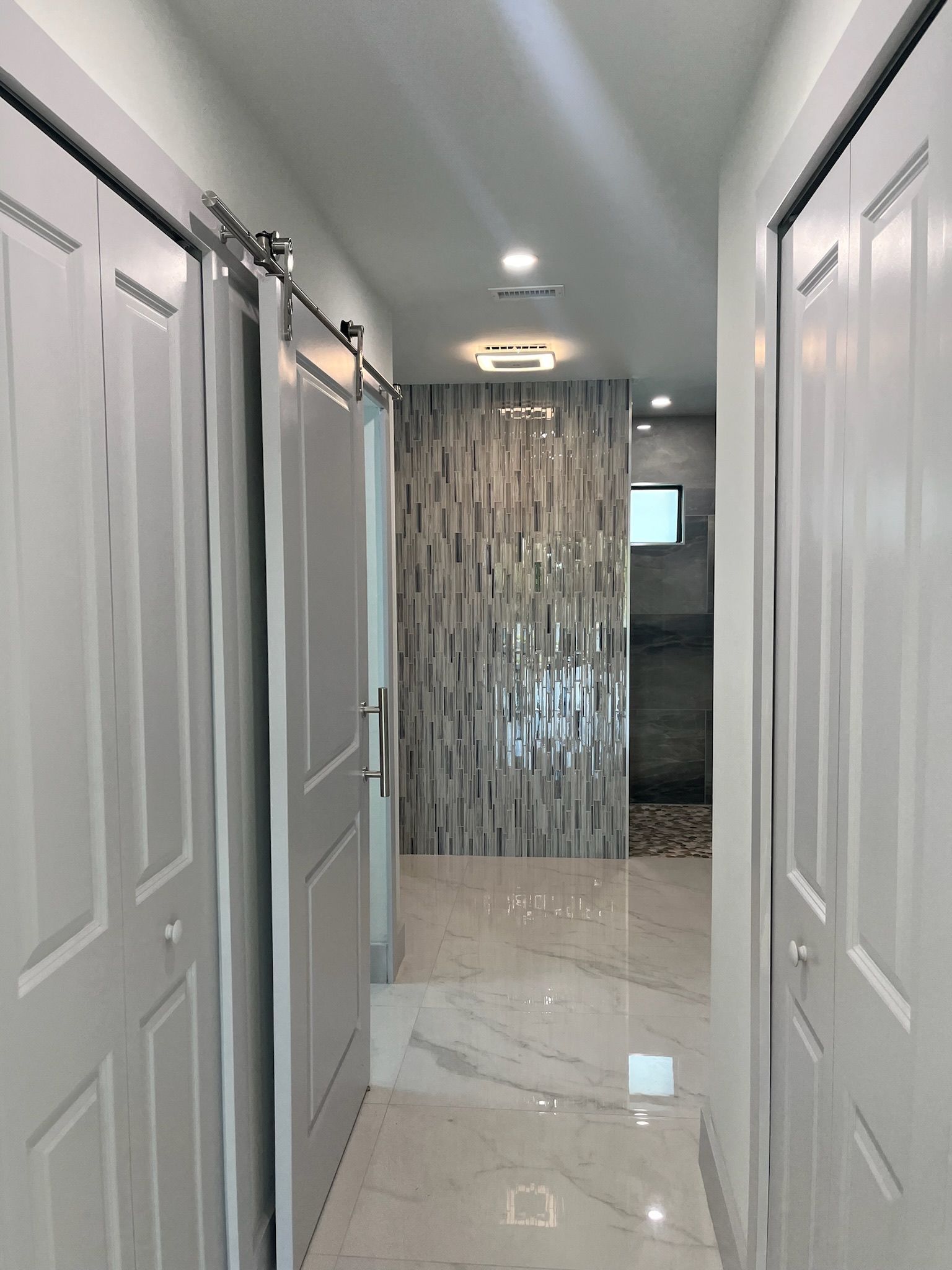 Hallway with white doors and marble floor, leading to a shower with decorative tile.