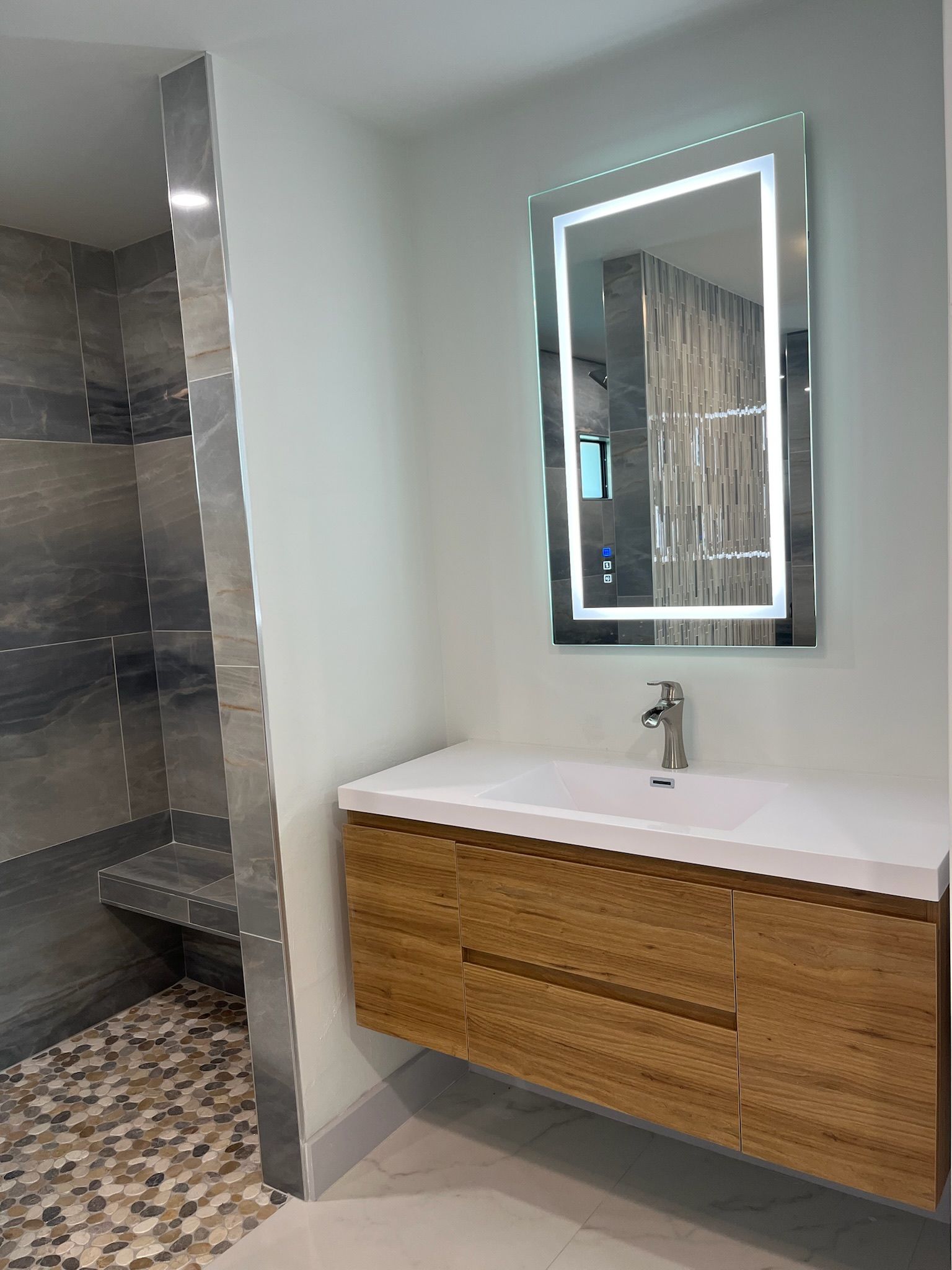 Modern bathroom with wood vanity, illuminated mirror, and tiled shower.