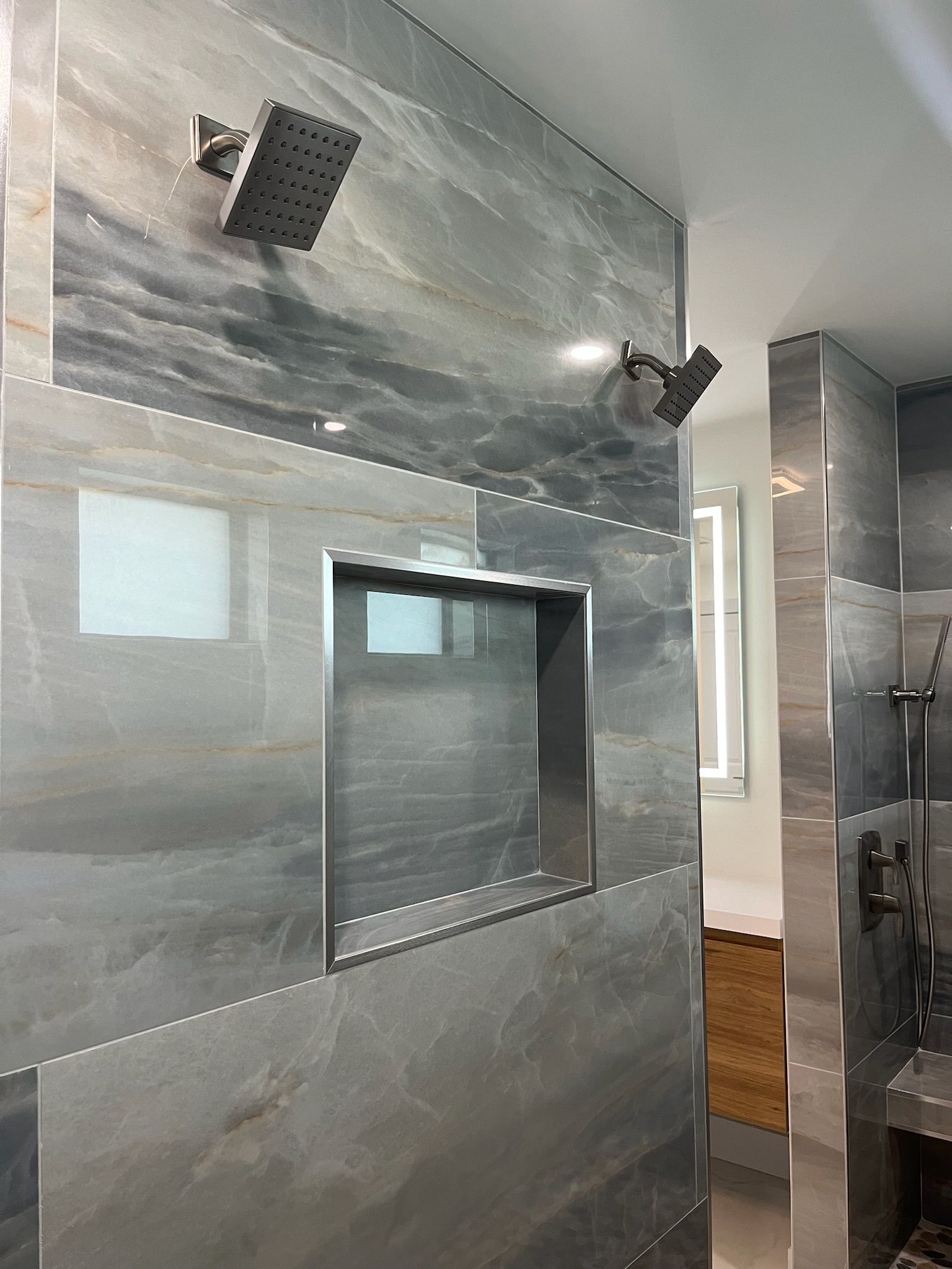 Grey-tiled shower with two showerheads, a recessed shelf, and stainless steel trim.
