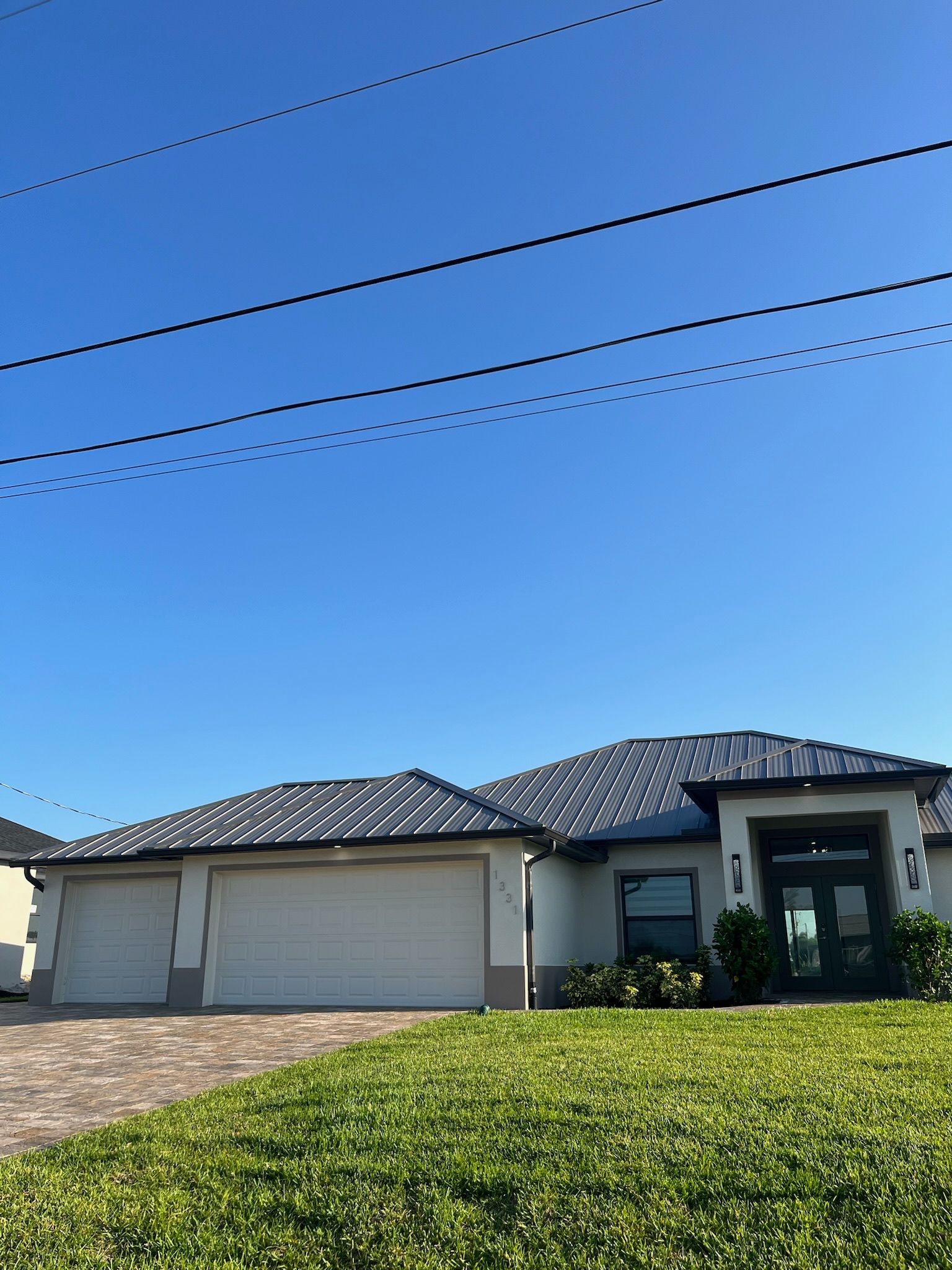 A light-colored house with a dark roof and three-car garage, under a bright blue sky.