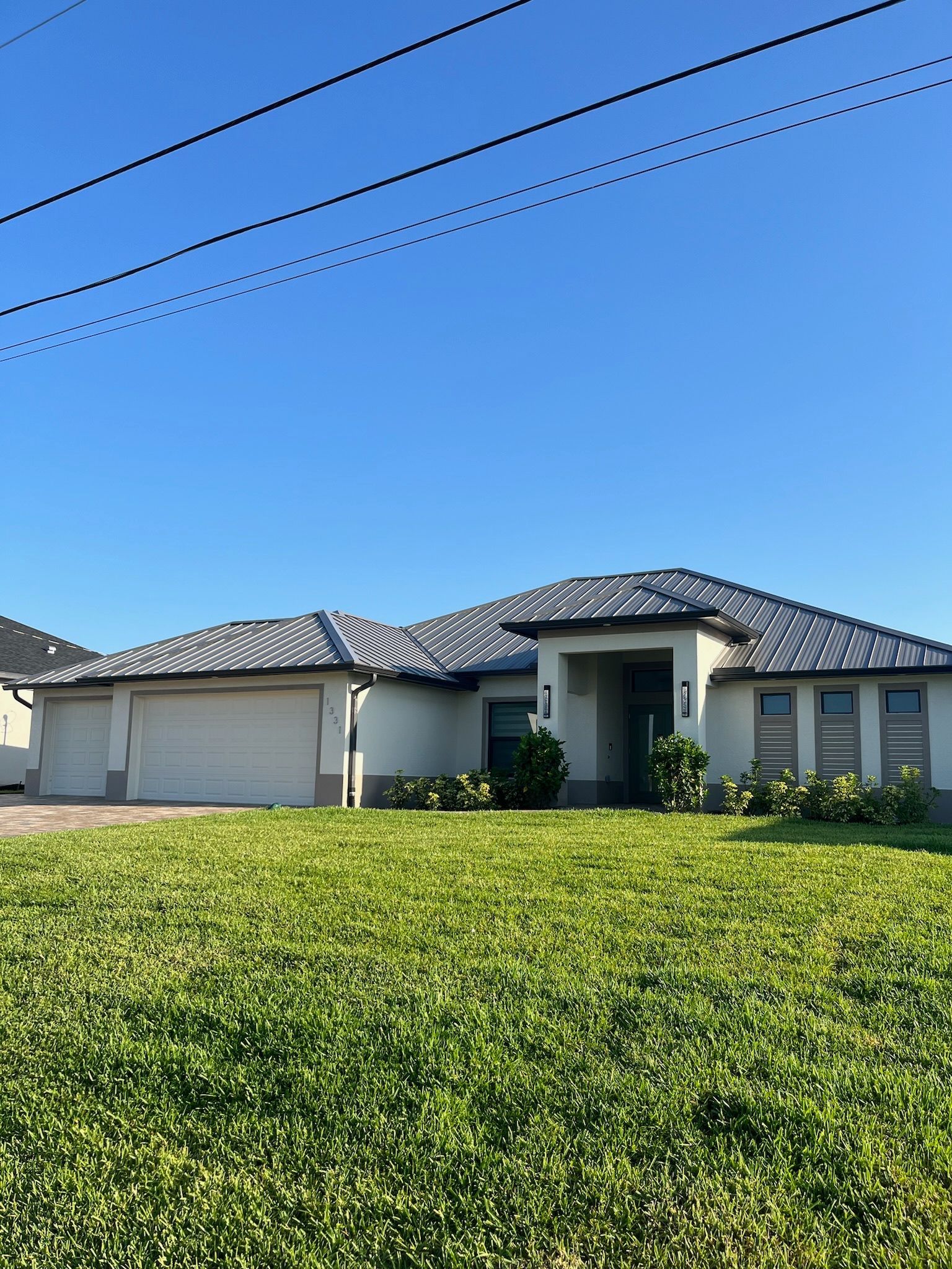A cream-colored house with a gray tile roof and green lawn under a blue sky.