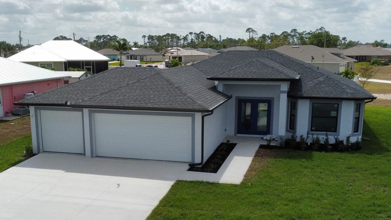 A light blue house with a dark gray roof, two-car garage, and blue front door, located in a suburban neighborhood.
