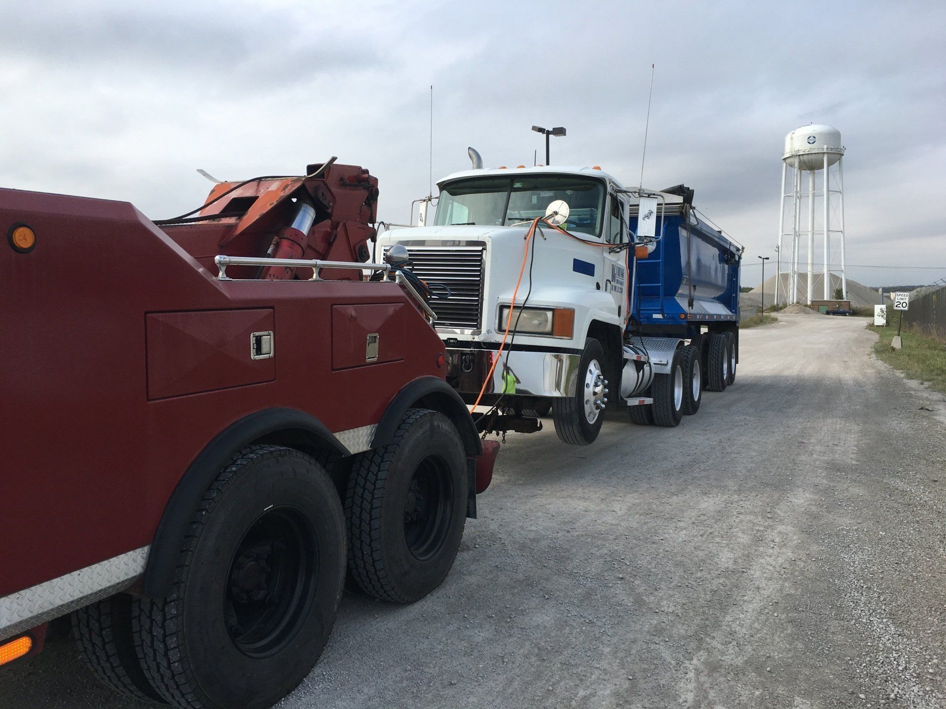 A tow truck is towing a dump truck on a gravel road.