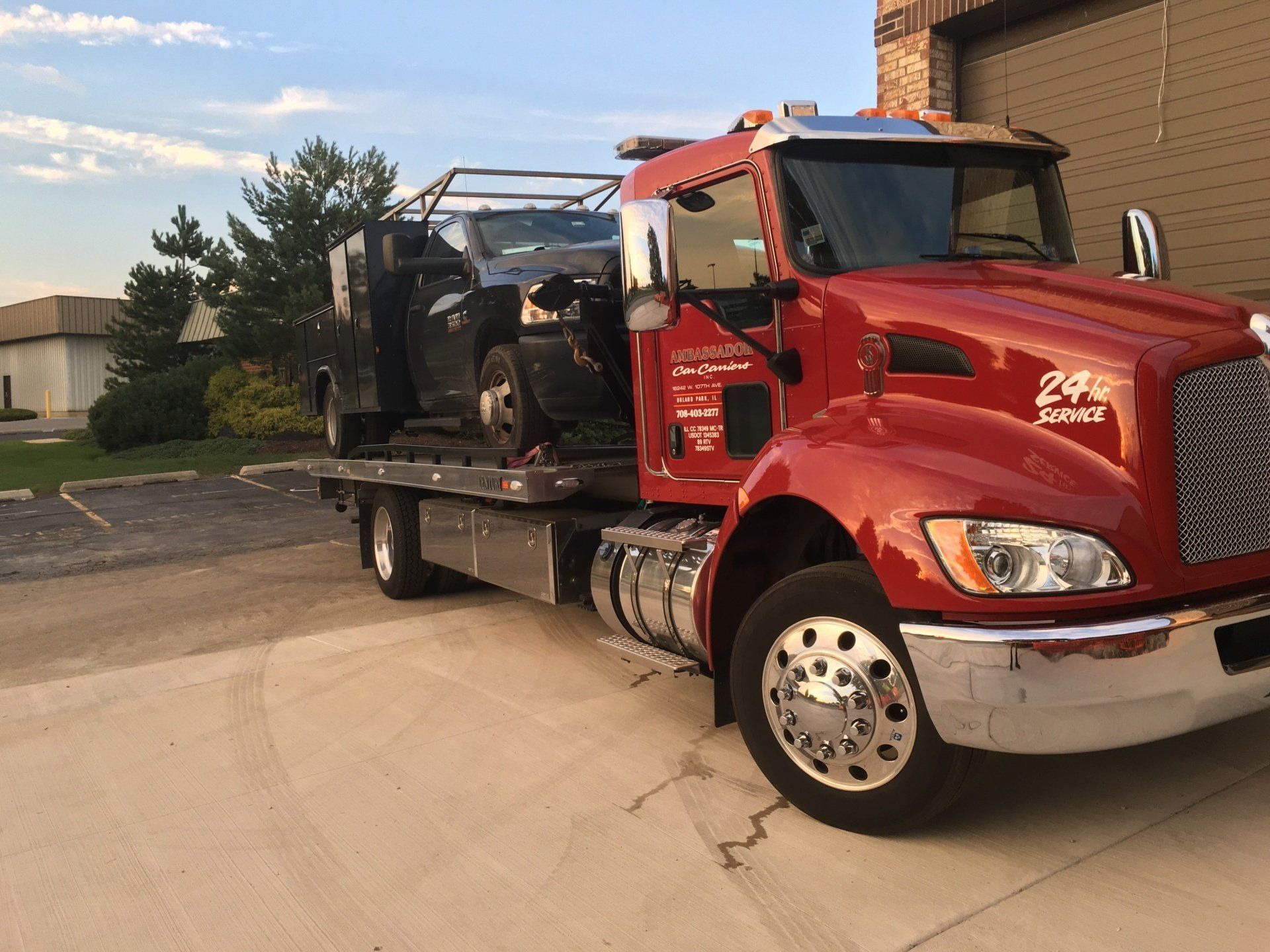 A red tow truck with a car on the back is parked in a driveway.