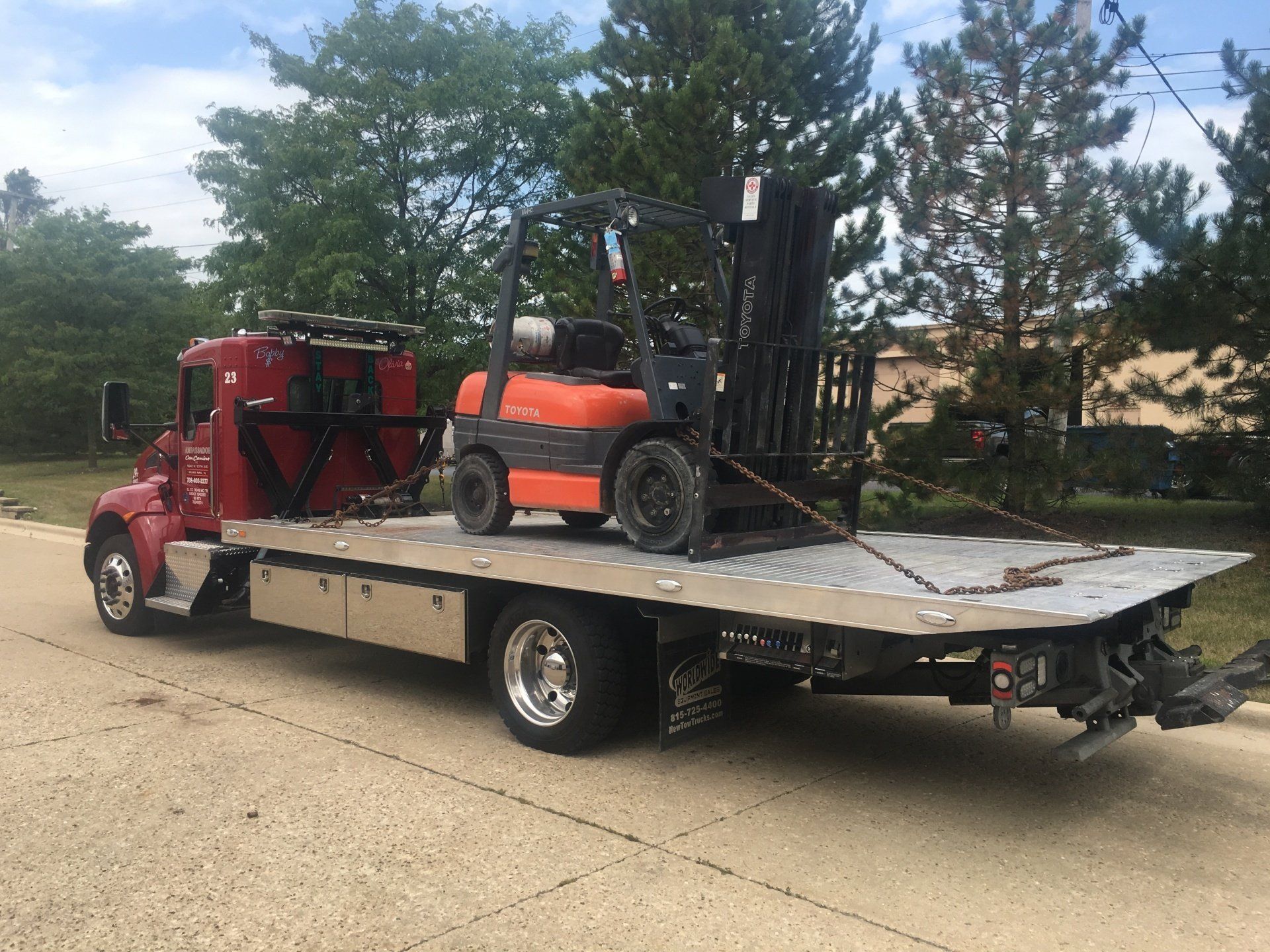 A red tow truck is carrying a forklift on the back of it.