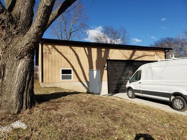 A white van is parked in front of a garage next to a tree.