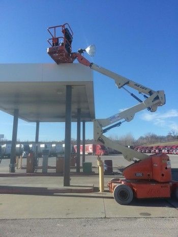 A man is working on the roof of a gas station with a crane.