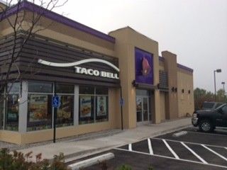 A taco bell restaurant with a parking lot in front of it