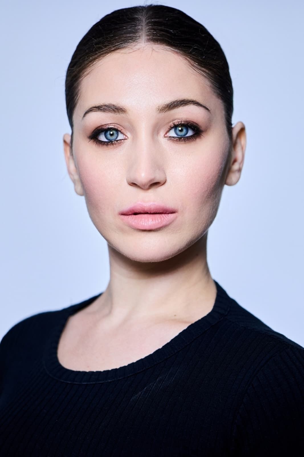 Una donna con lunghi capelli scuri sorride, indossa un top nero e un rossetto scuro.