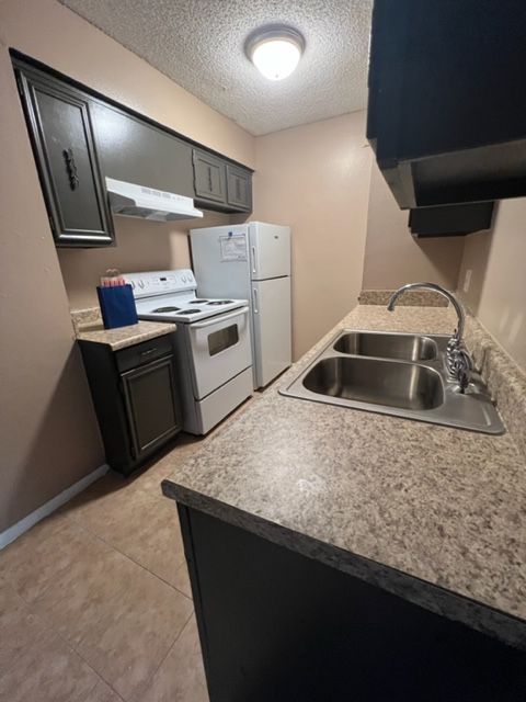 Small kitchen with white appliances, dark cabinets, and a double sink.