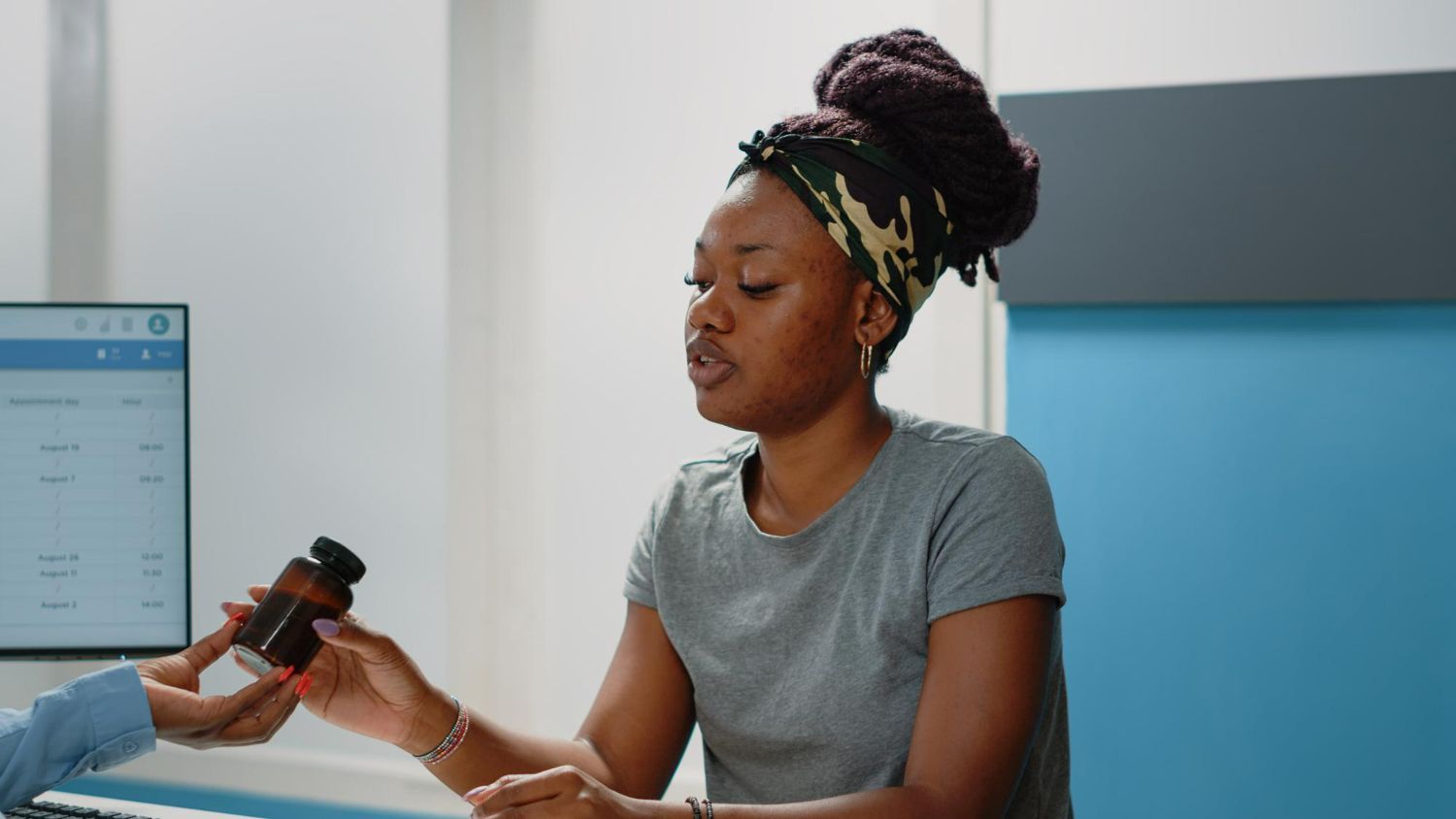 Woman receiving medication bottle from someone in medical setting.