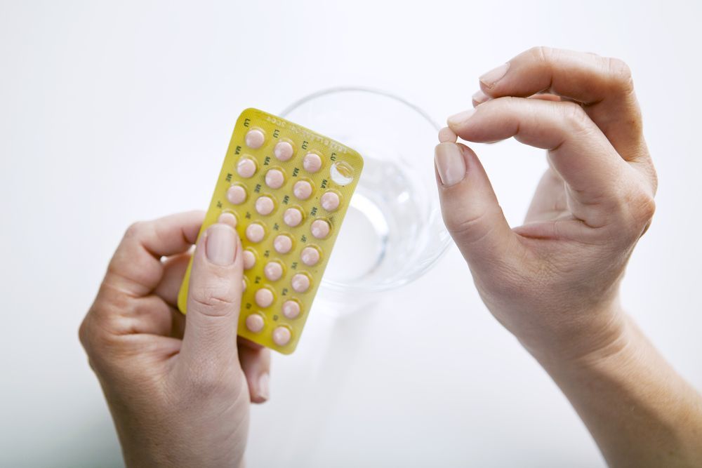 Hands holding birth control pills and a glass of water.
