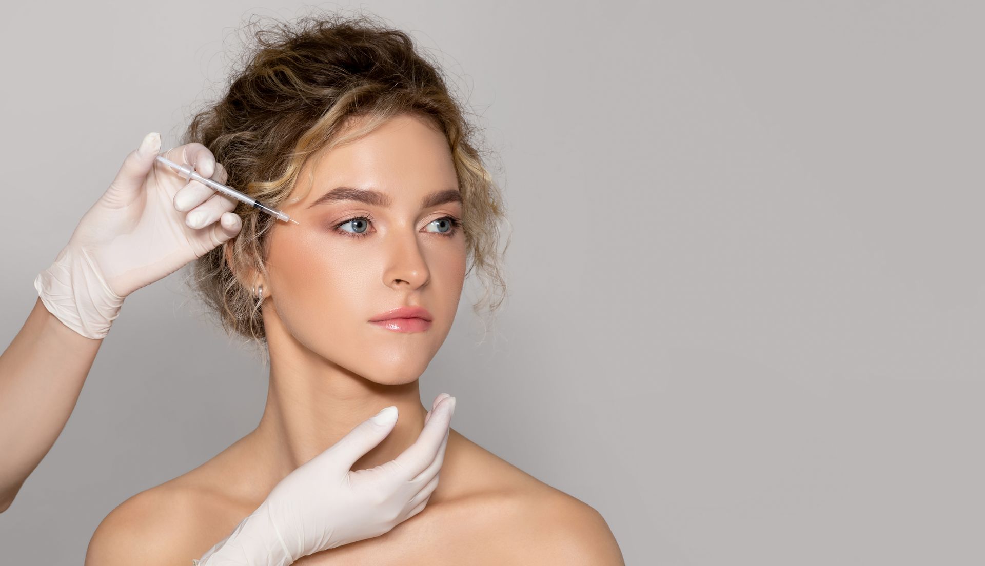 Gloved hands holding a cosmetic syringe near a woman’s face during a treatment