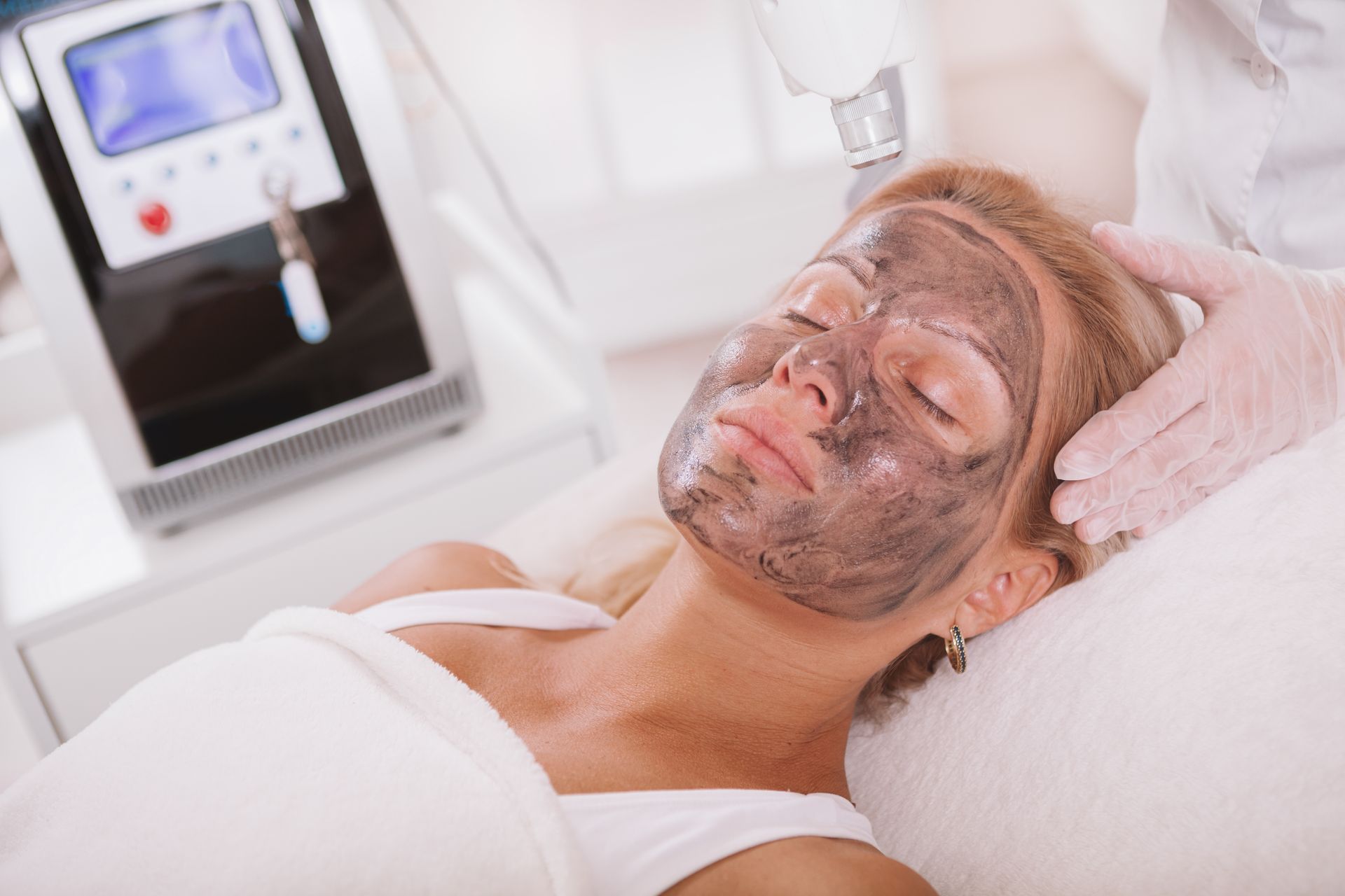 A woman is laying on a bed with a charcoal mask on her face.