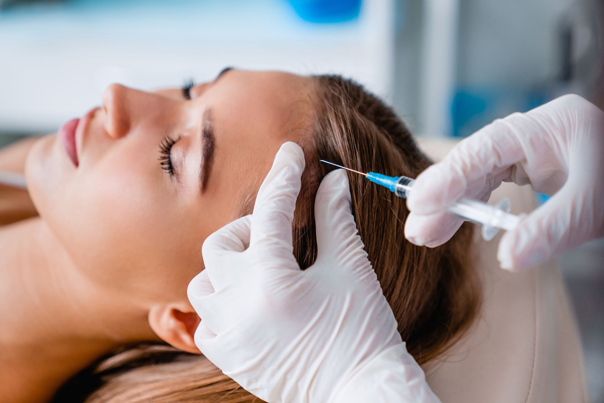 Gloved practitioner administering a facial injection to a reclining patient in a clinical setting