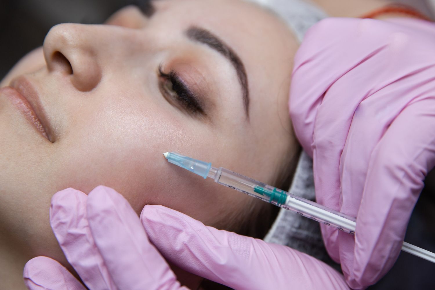 Person receiving a facial injection; pink gloves, needle near cheek.