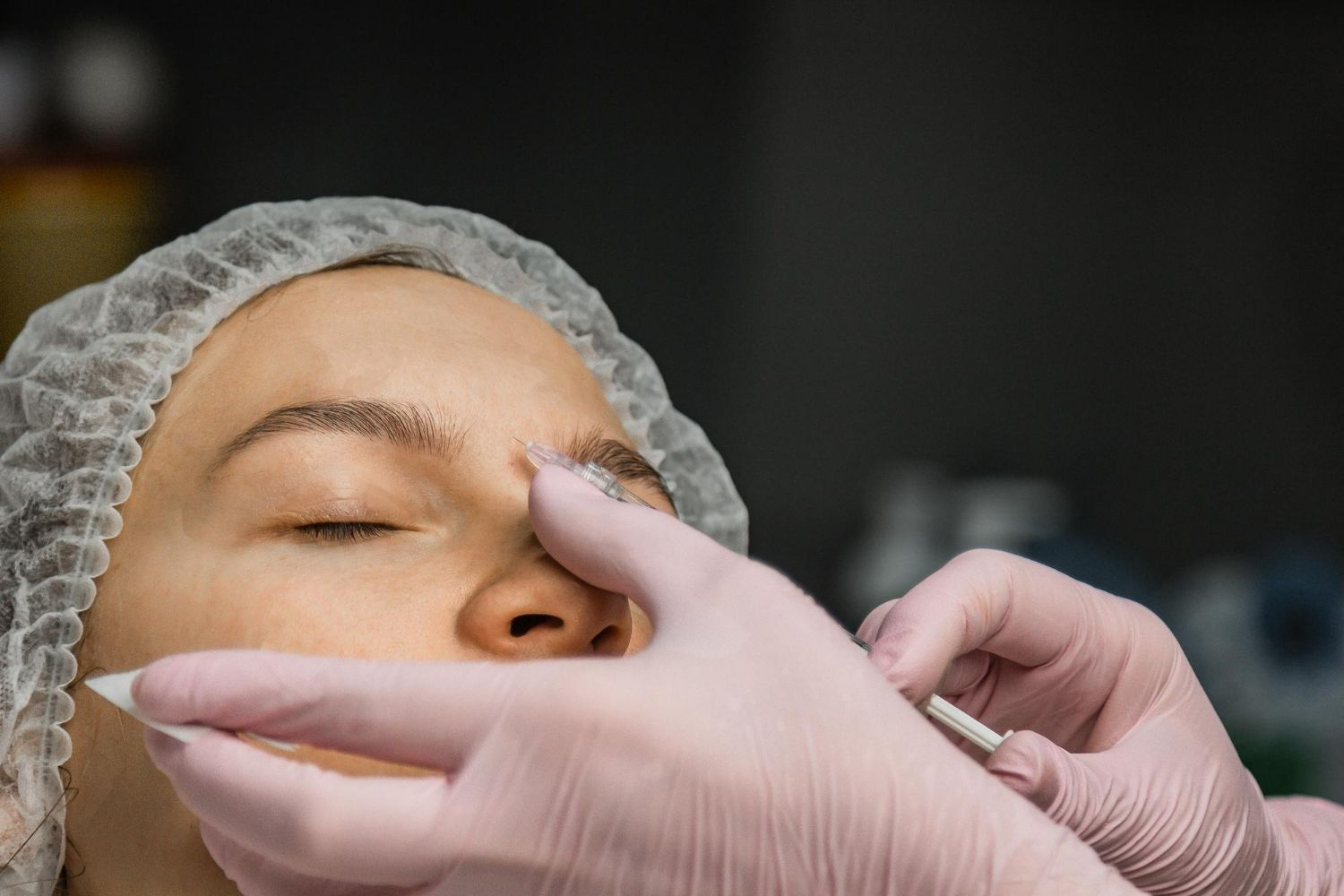 Woman receiving cosmetic procedure on her face, hands in pink gloves.