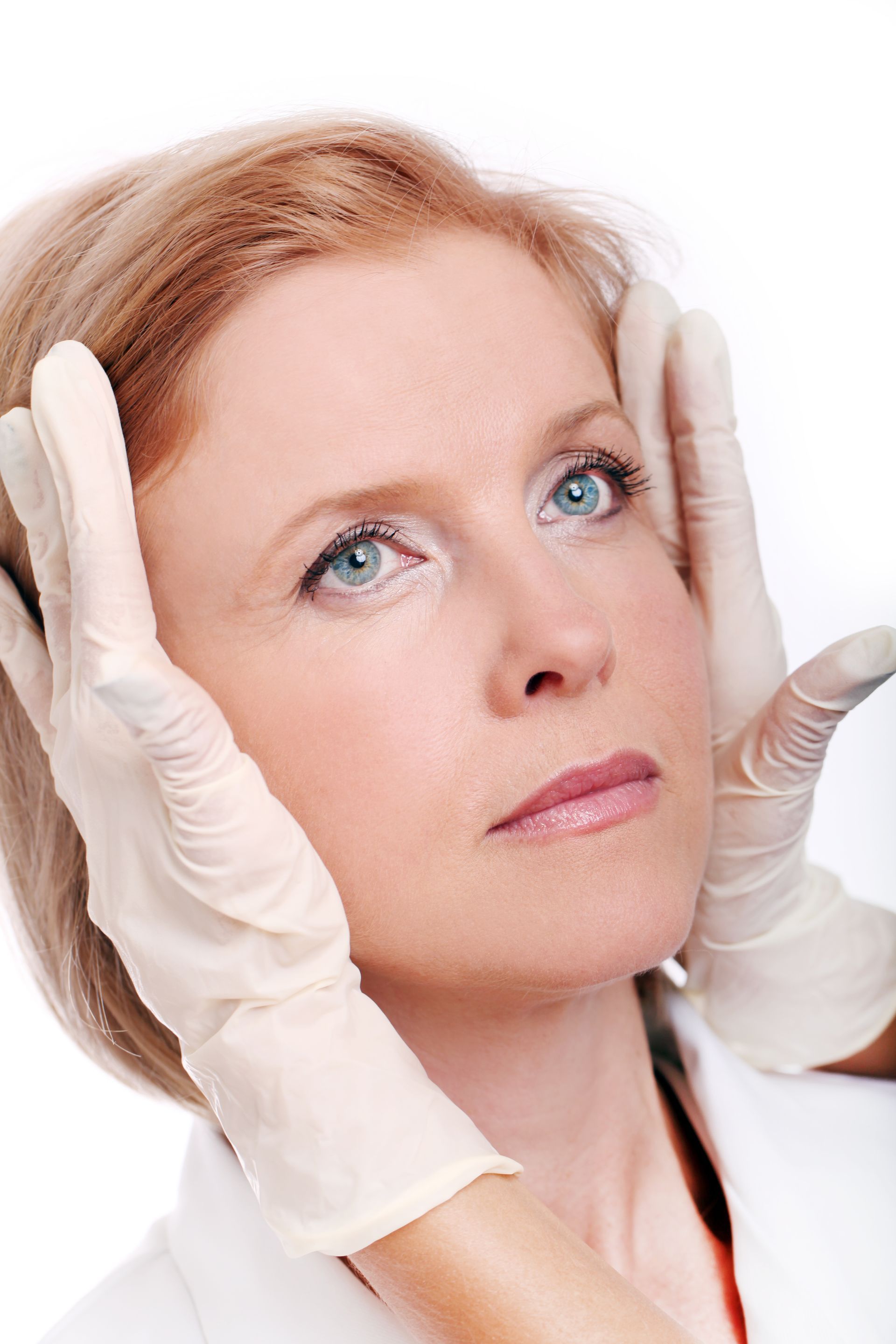 A woman is getting her face examined by a doctor wearing gloves.