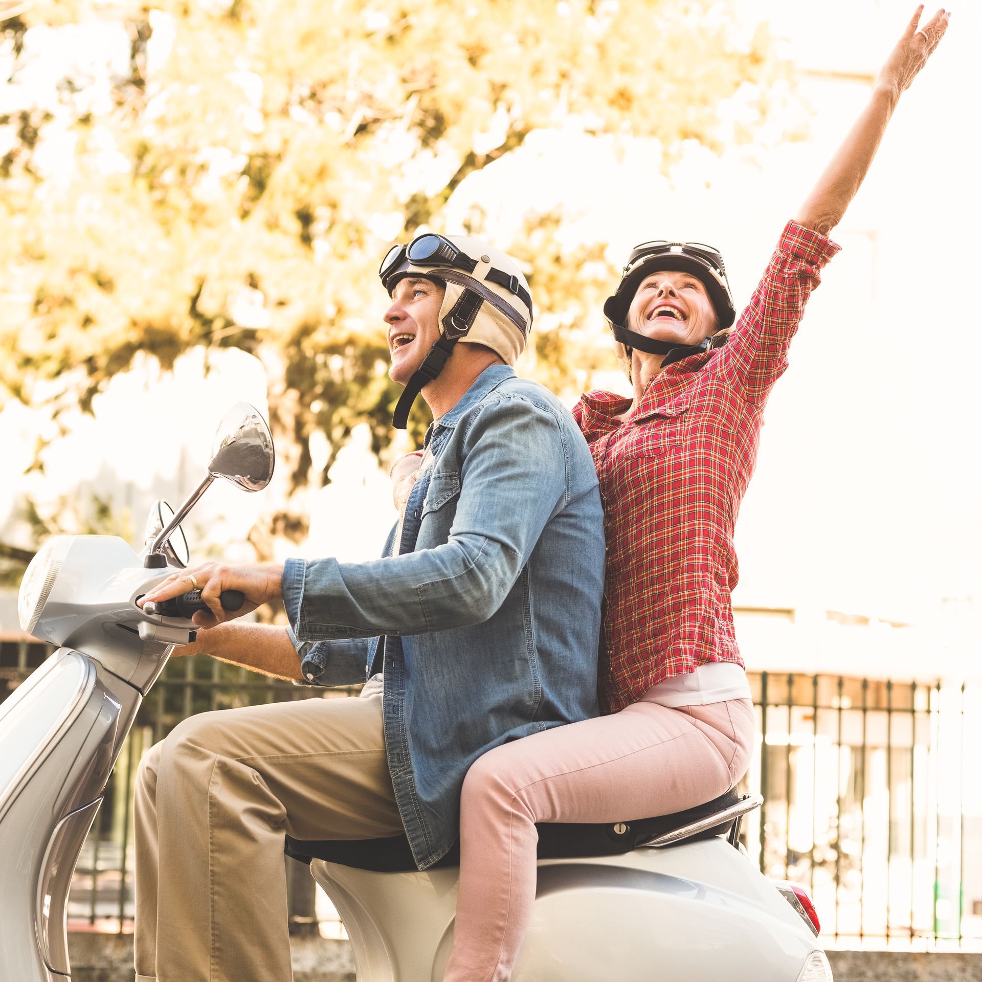 A man and a woman are riding a scooter with their arms in the air.