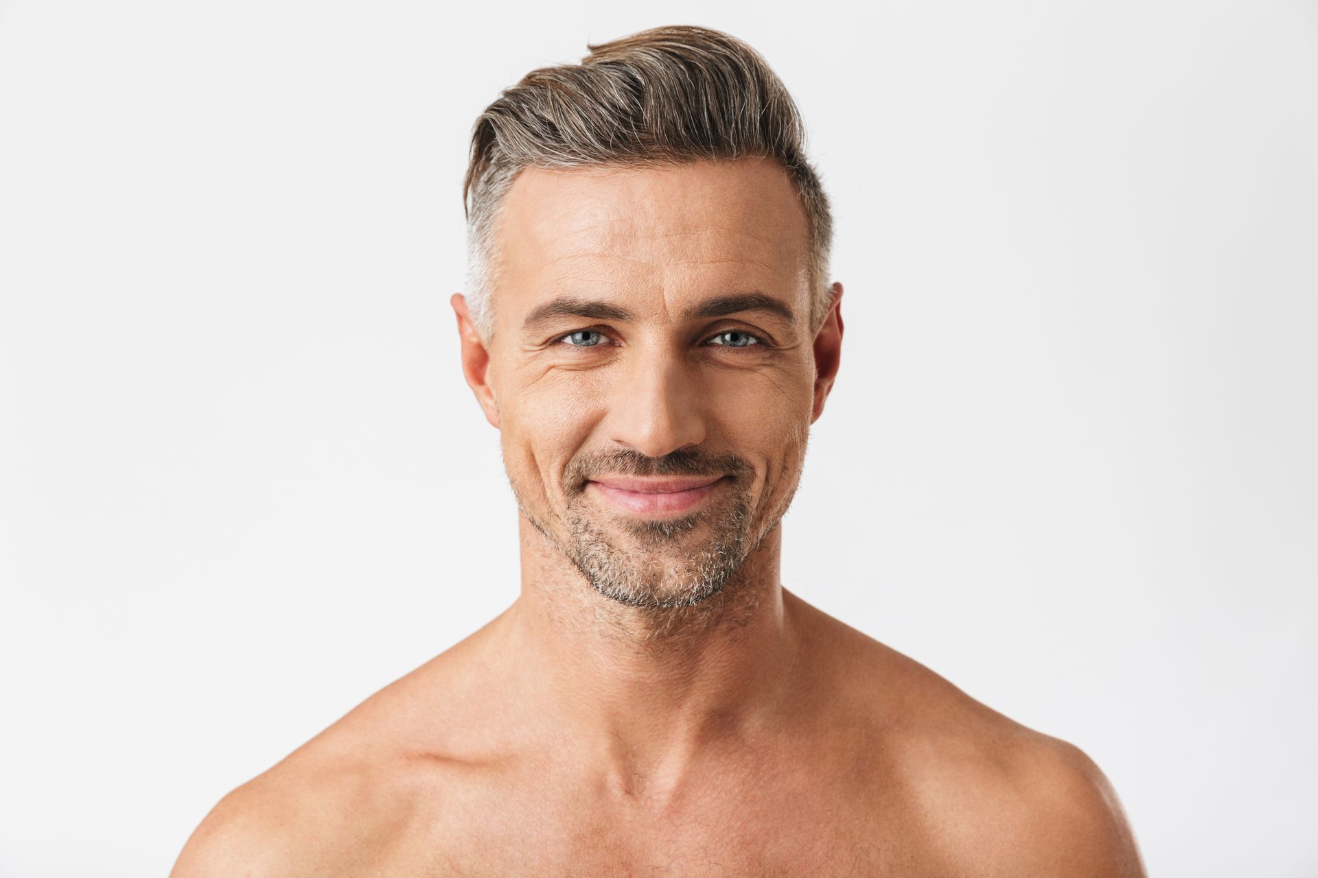 A shirtless man with a beard is smiling and looking at the camera.