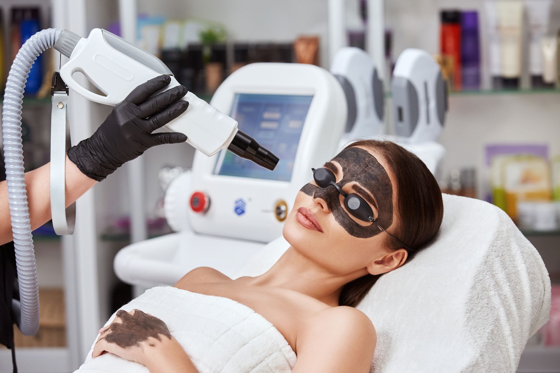 A woman is getting a black mask on her face in a beauty salon.