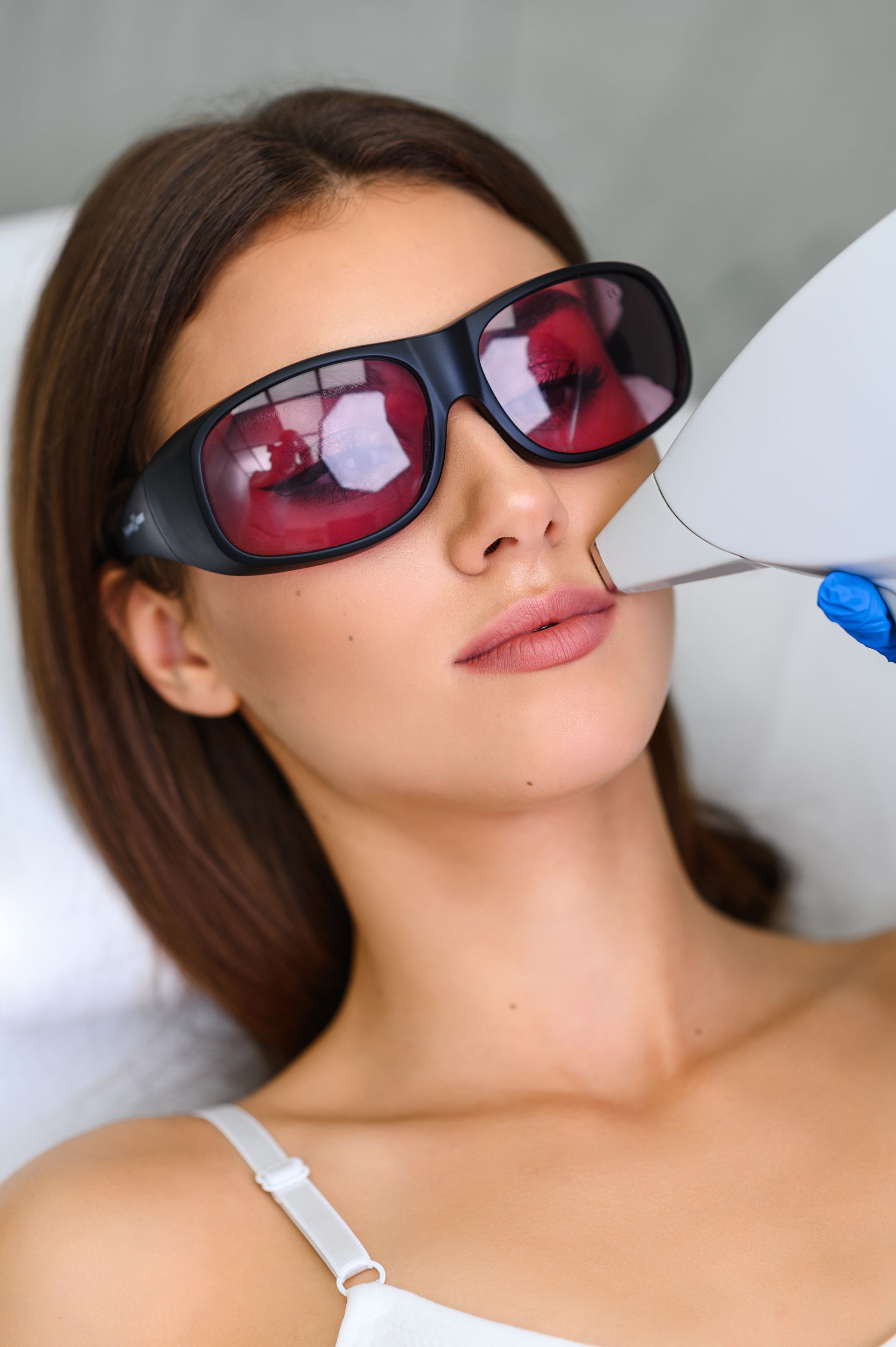 A woman wearing sunglasses is getting a laser hair removal treatment on her face.