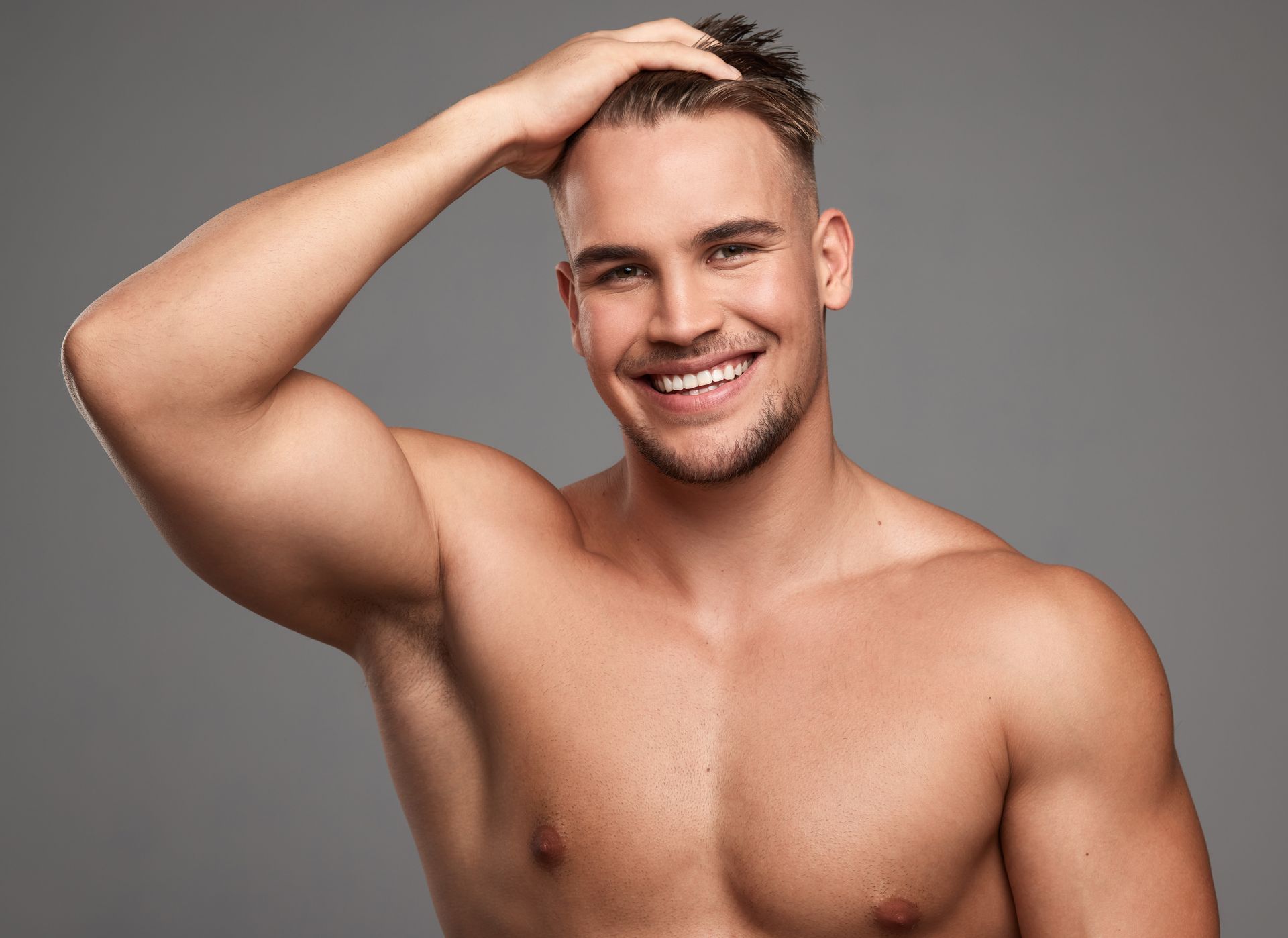 A shirtless man is smiling and touching his hair.