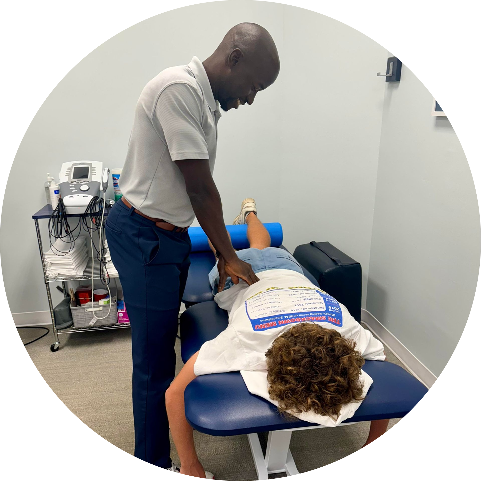 A healthcare professional treating a patient lying on a therapy table; white room setting.