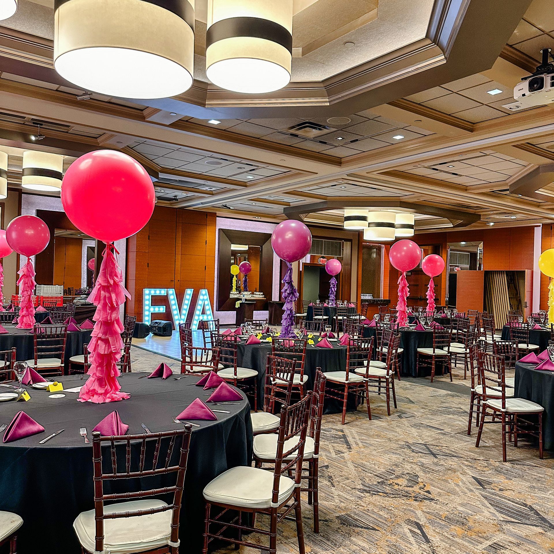 A large room with tables and chairs decorated for a party with balloons and a sign that says eva
