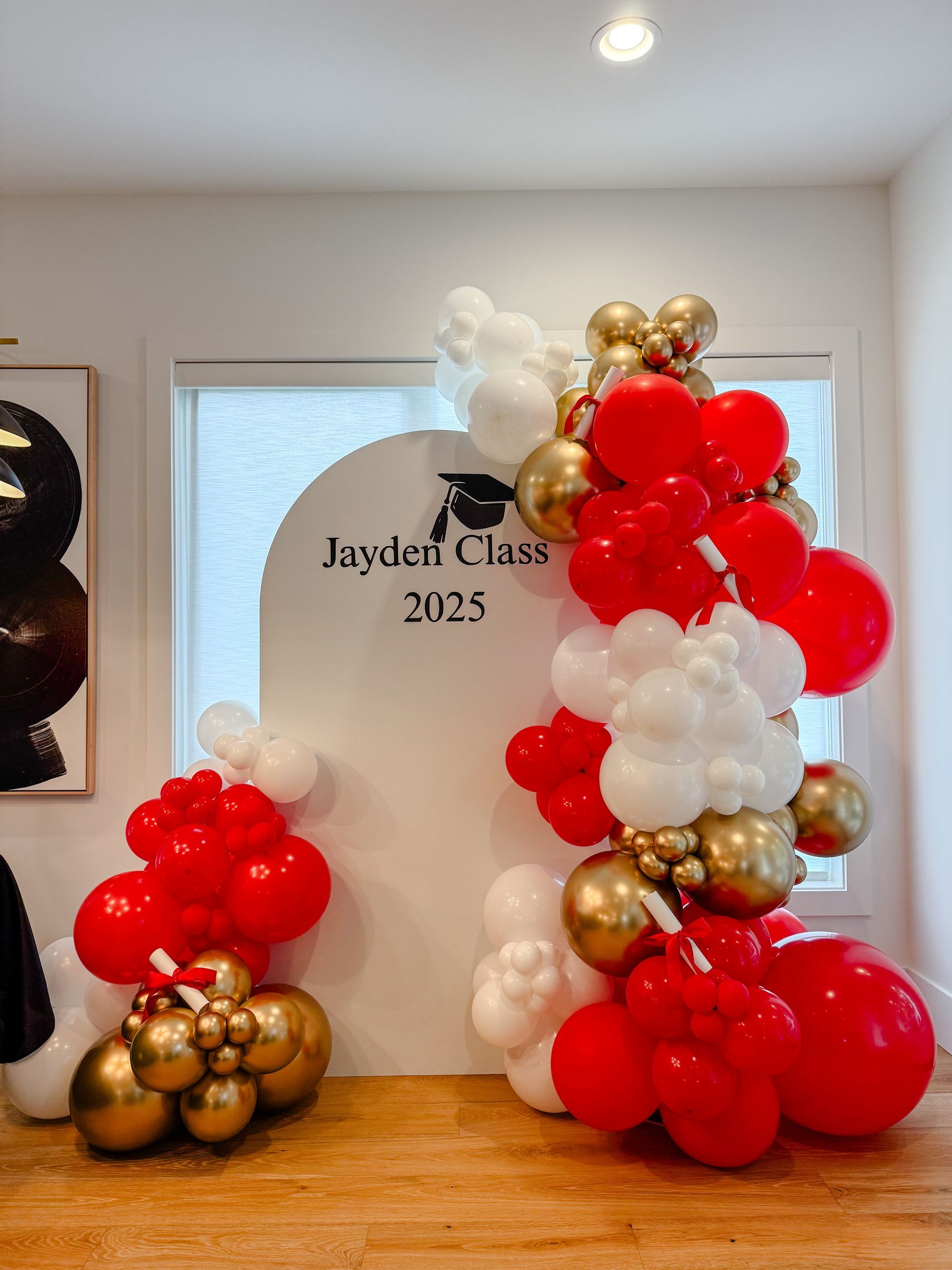 Balloon arch in red, white, and gold, next to a sign for Jaylieri Class of 2025.