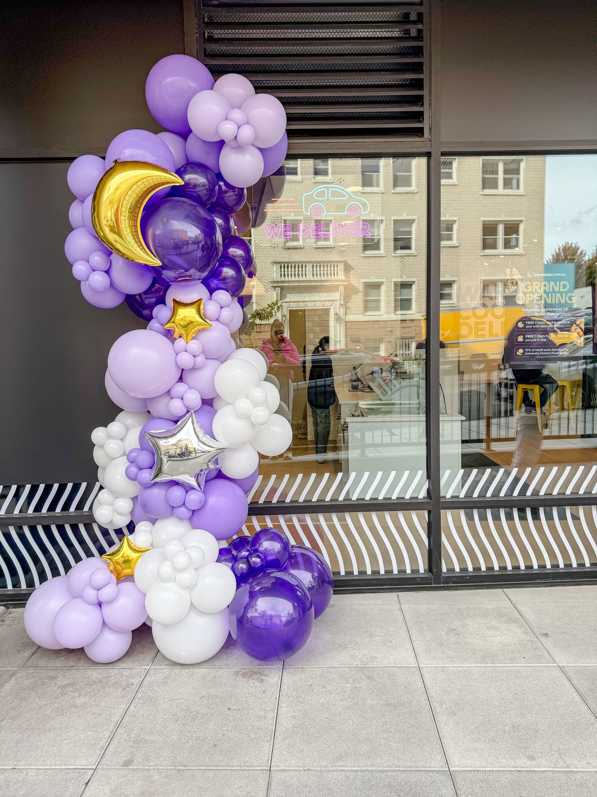 A bunch of purple and white balloons are sitting in front of a building.